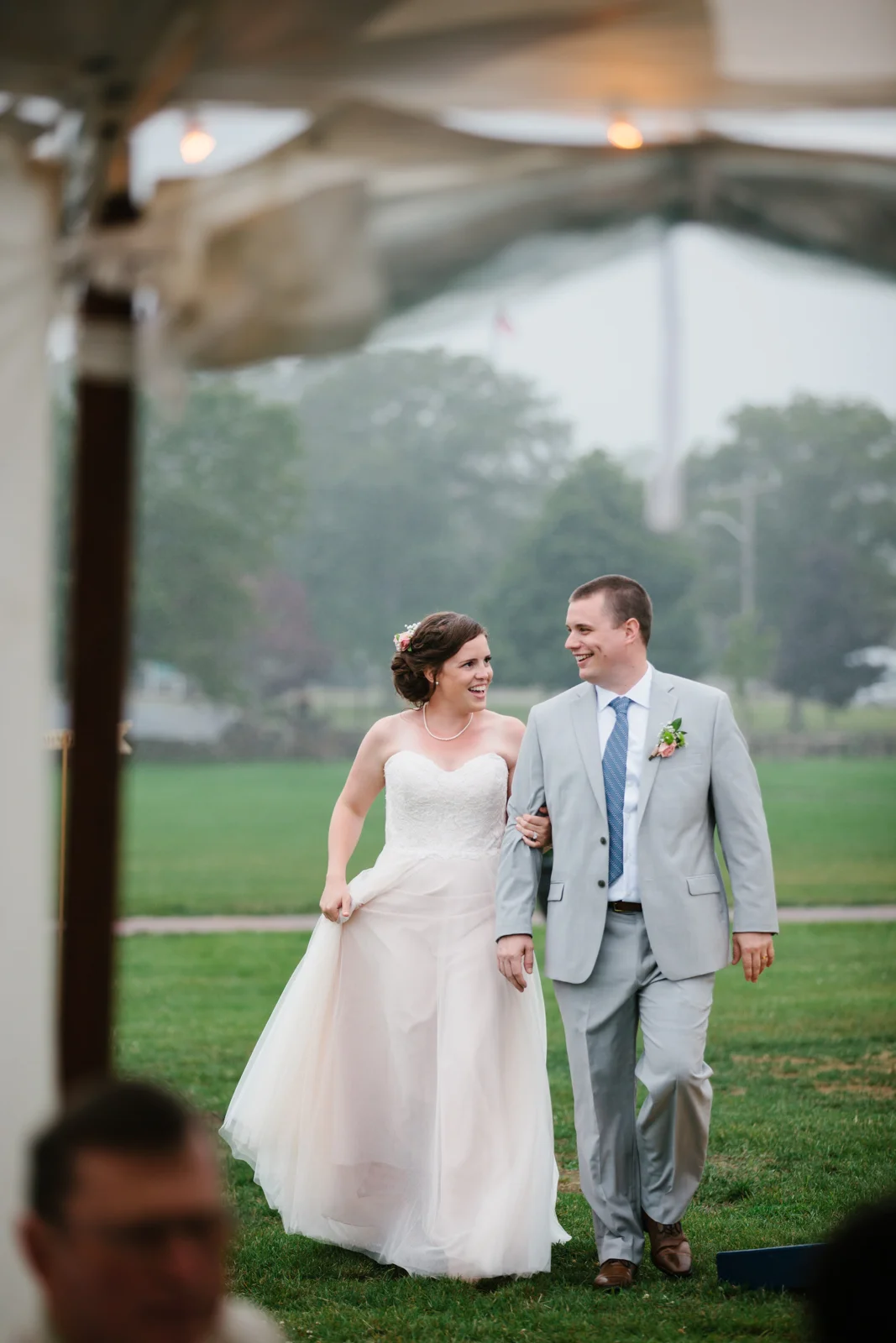 A bride and groom walking arm in arm outdoors, smiling and looking at each other, during their wedding celebration.
