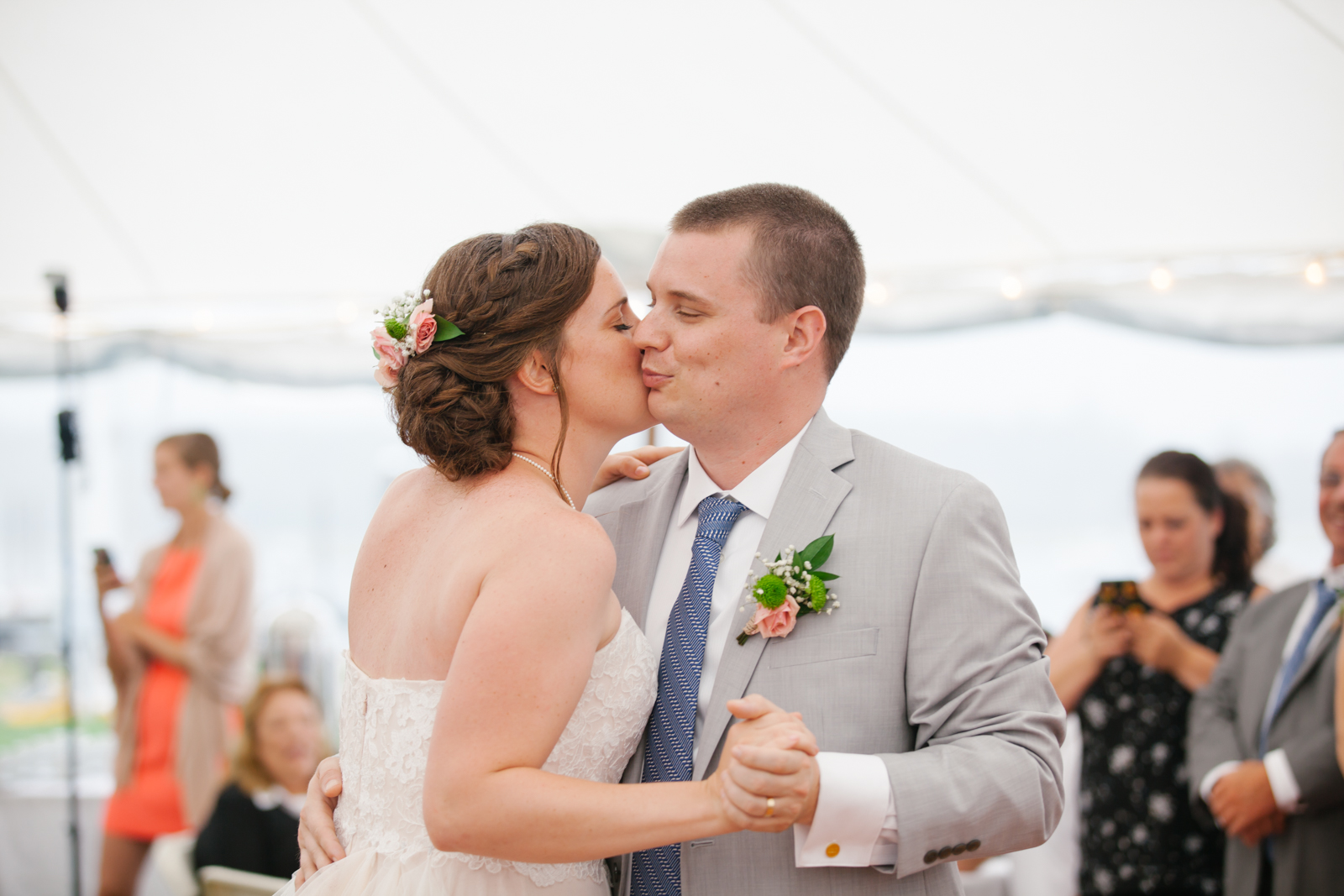 A bride and groom sharing a kiss and dance at their wedding reception, with guests in the background.