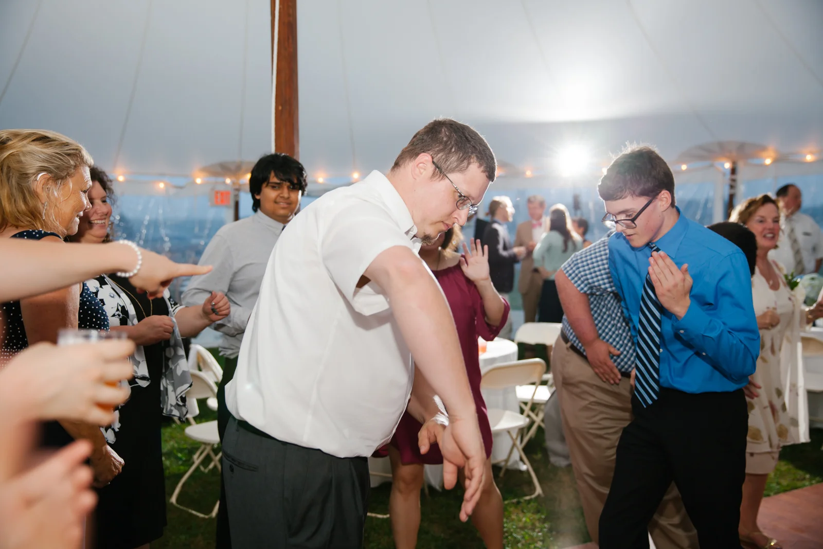 People dancing and enjoying themselves at a celebratory event under a large tent, with some individuals dancing and others clapping.