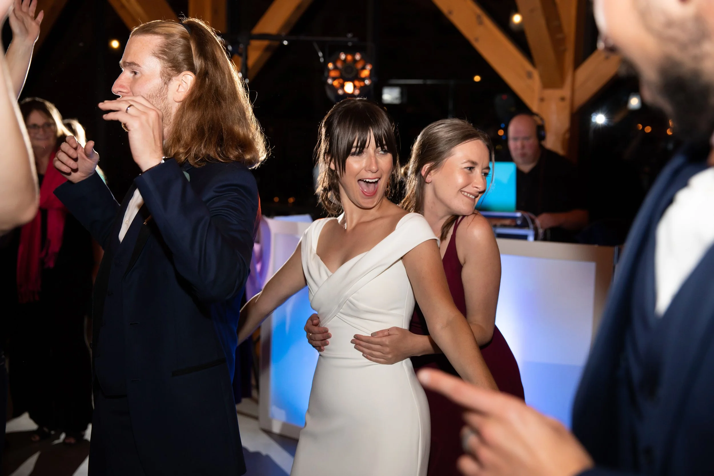 People dancing and laughing at a festive event with a DJ playing music in the background.