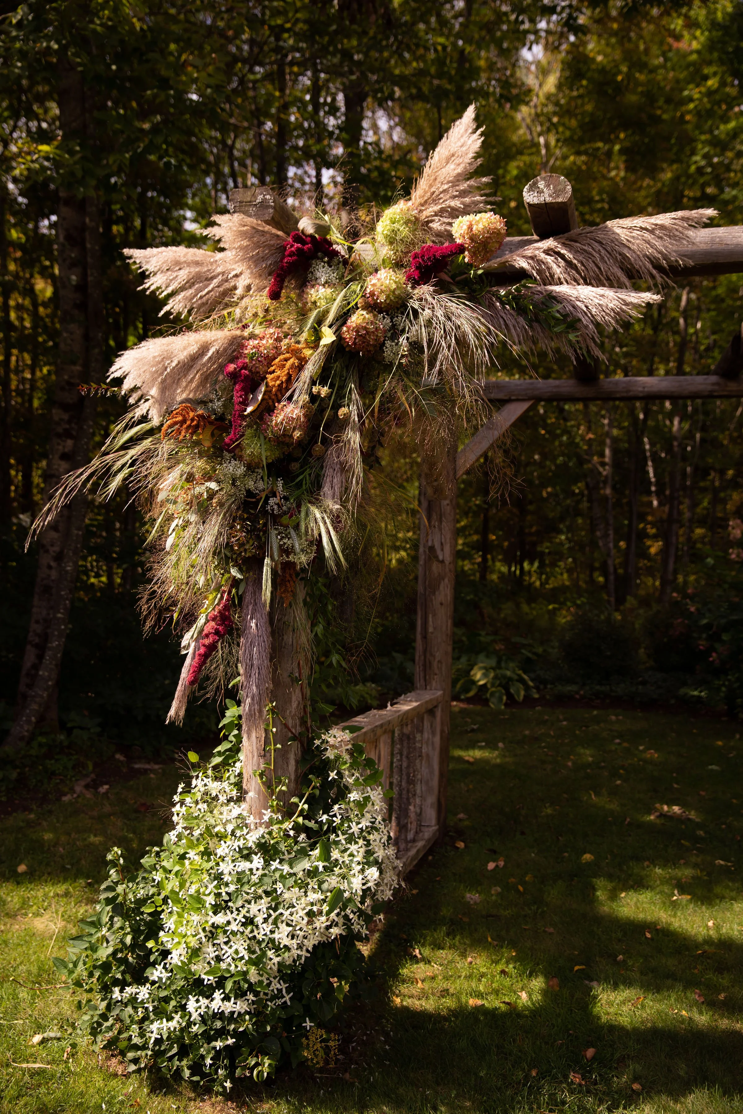Decorated wooden arch with floral arrangement, outdoor setting in a wooded area.