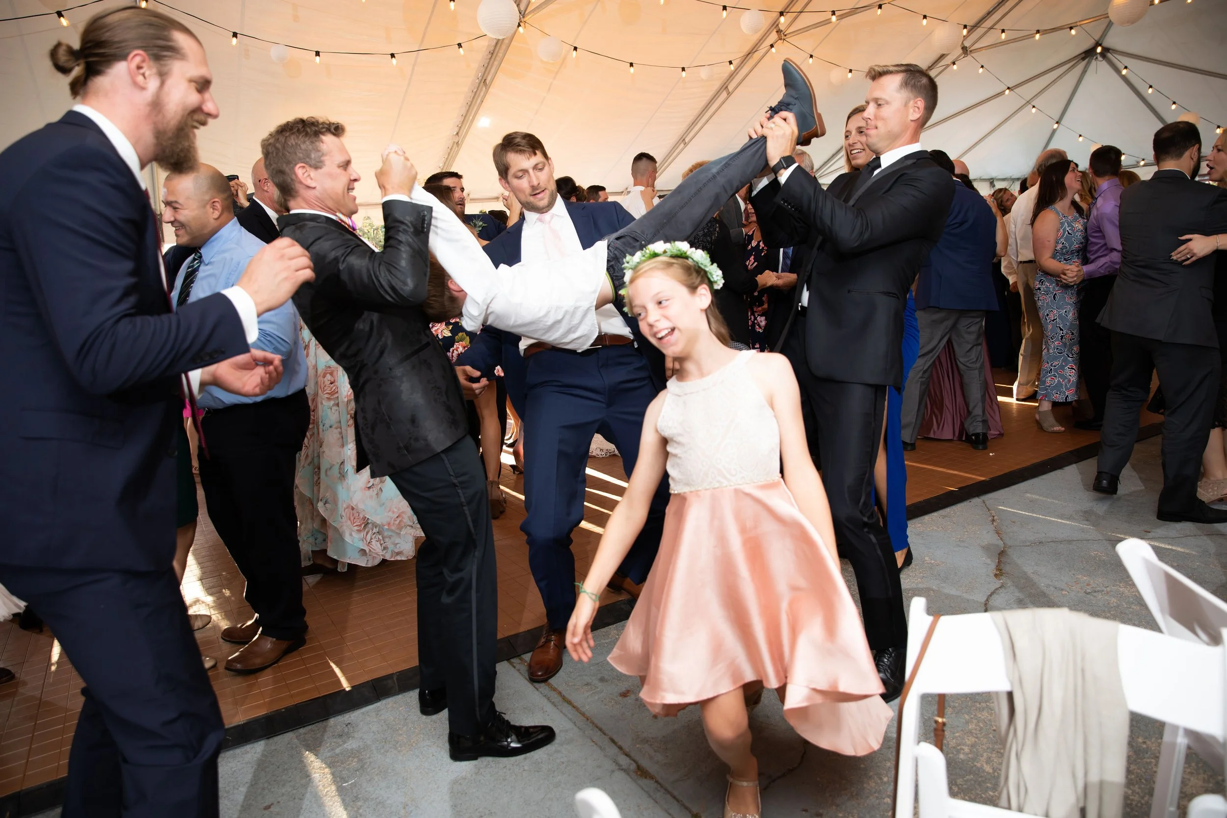 People dancing and having fun at a wedding reception, with someone being lifted and others smiling and enjoying the party.