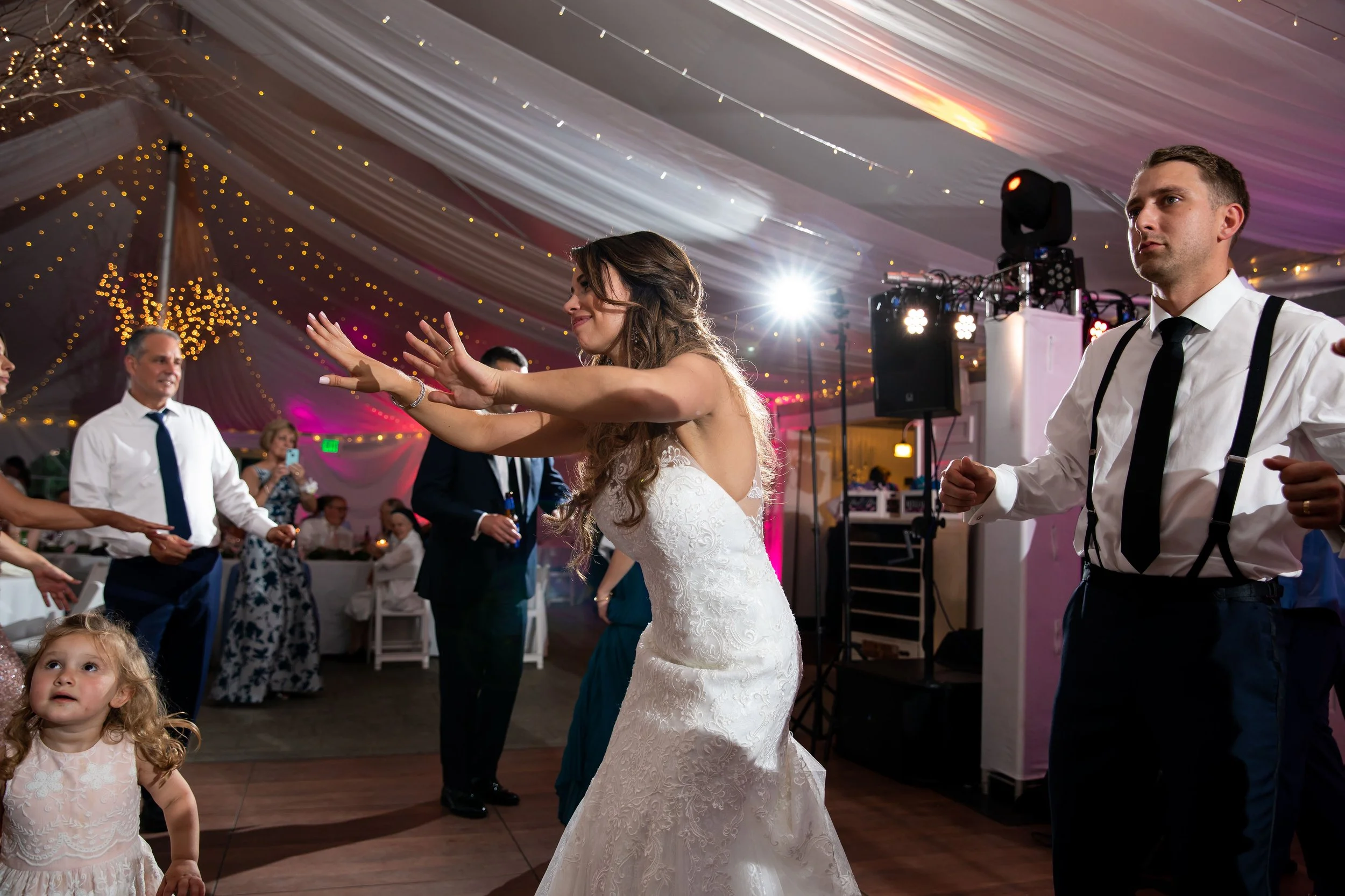 Wedding reception scene with bride dancing and guests enjoying in decorated tent.