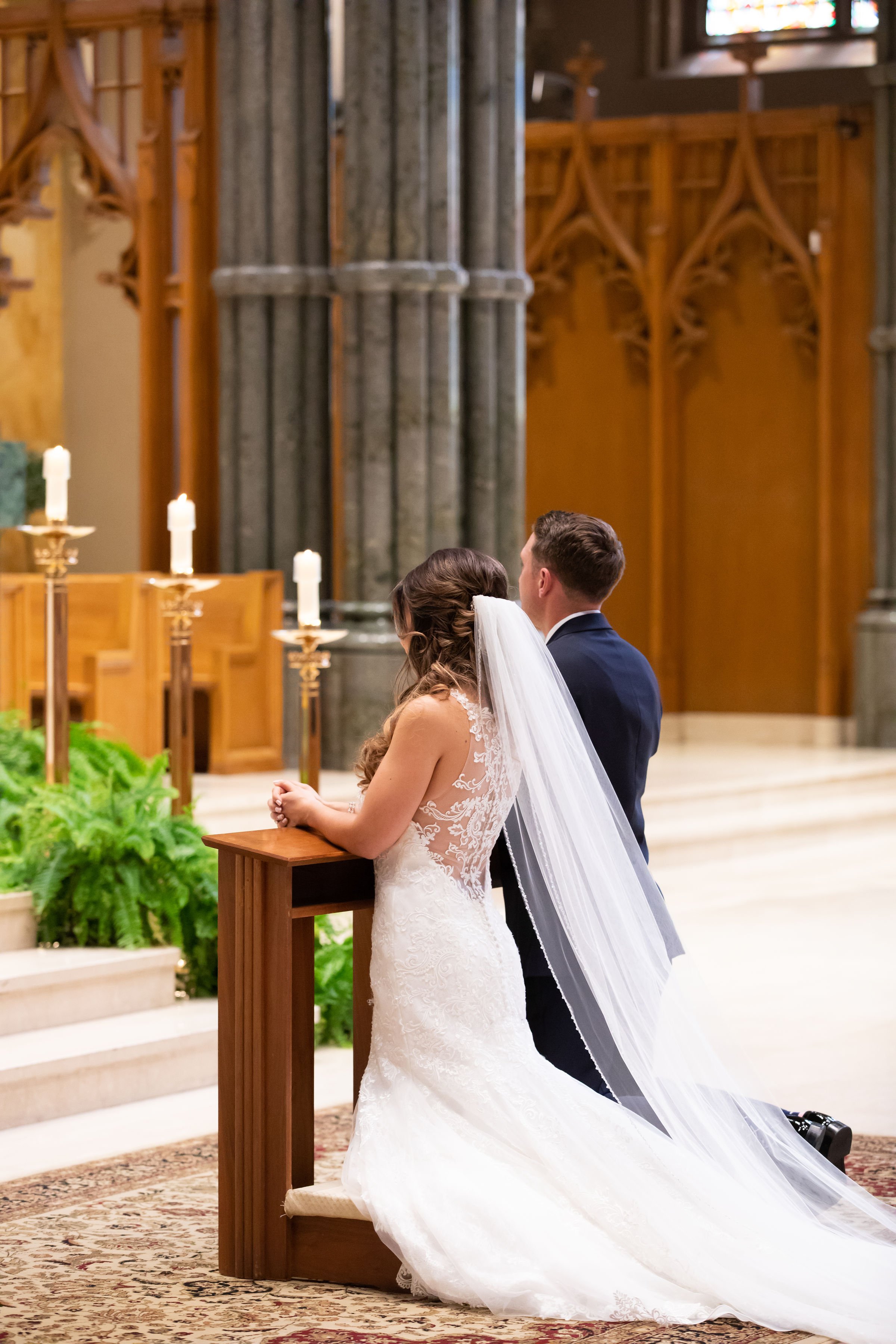A bride and groom kneeling at an altar during their wedding ceremony in a church.