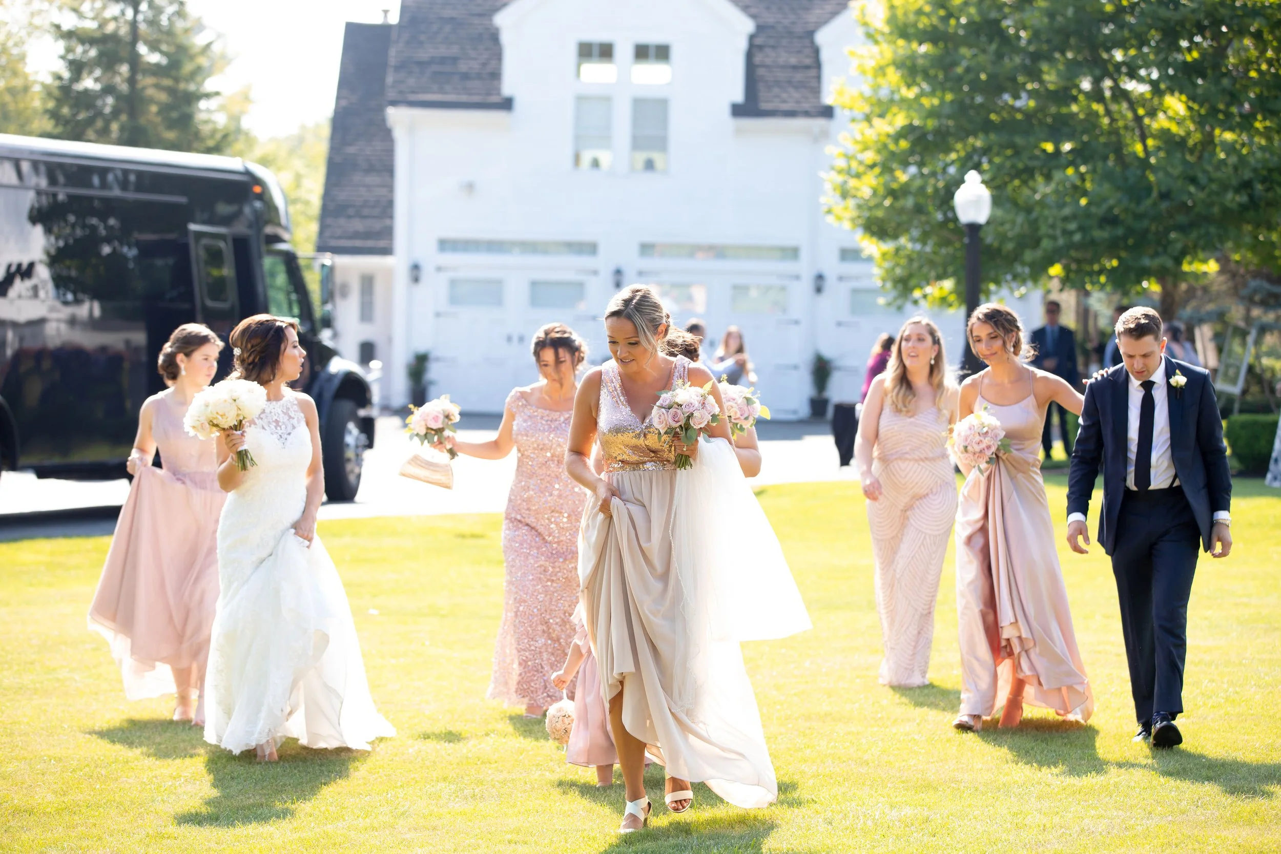 A bride walking in a garden with her bridesmaids and groomsmen during a wedding celebration.