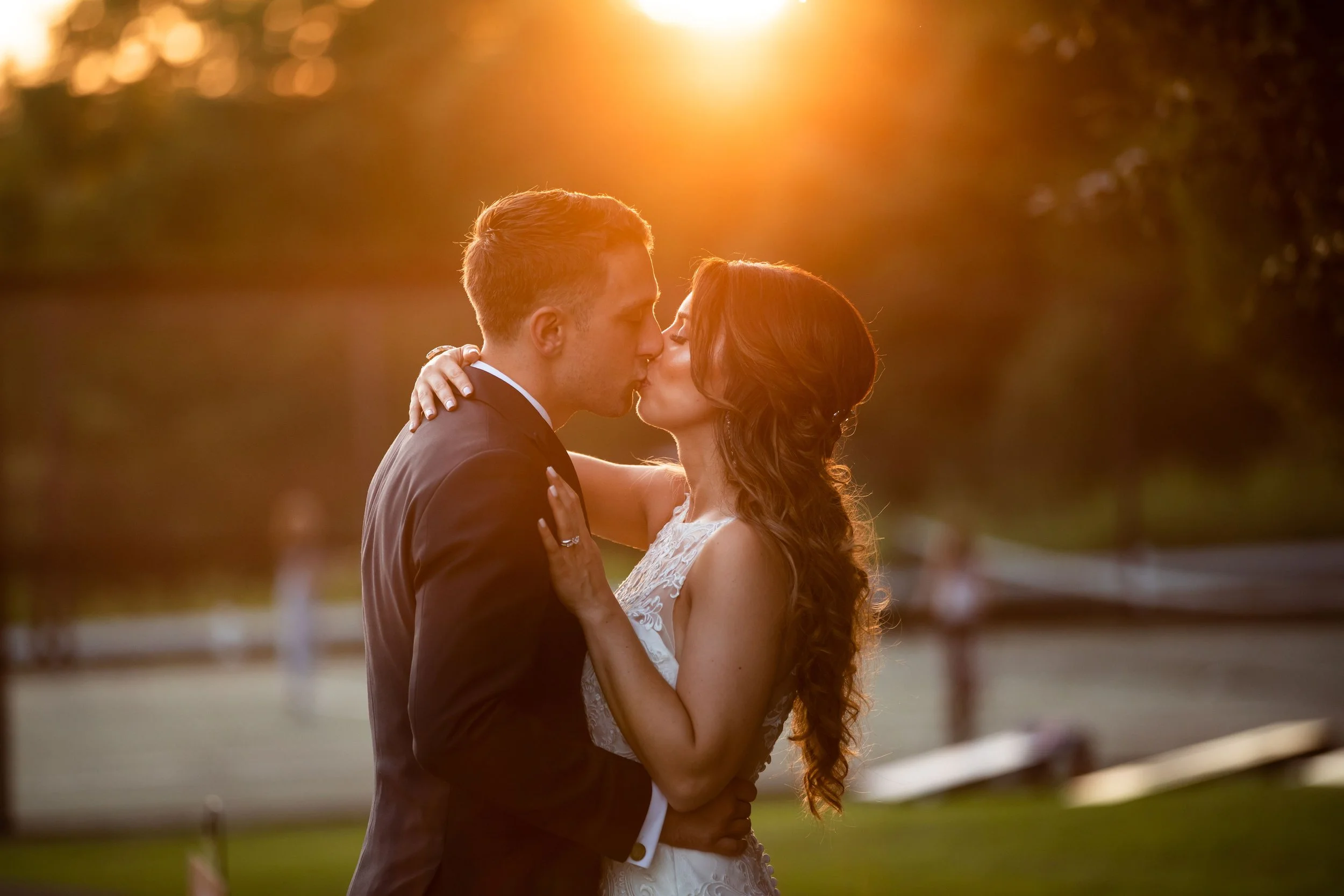 Couple in wedding attire sharing a kiss outdoors during sunset.