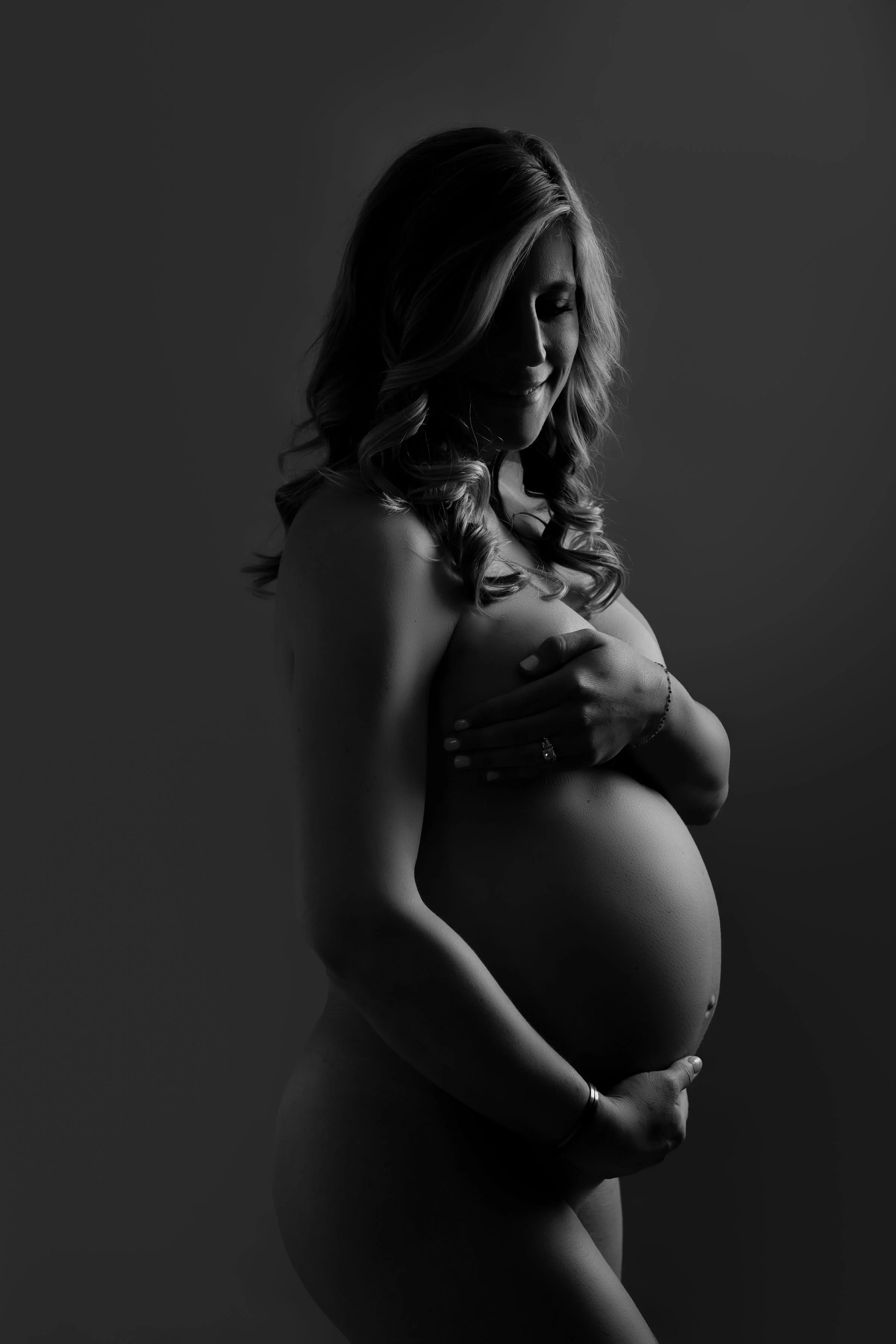 Black and white photo of a pregnant woman cradling her belly and smiling softly with eyes closed.