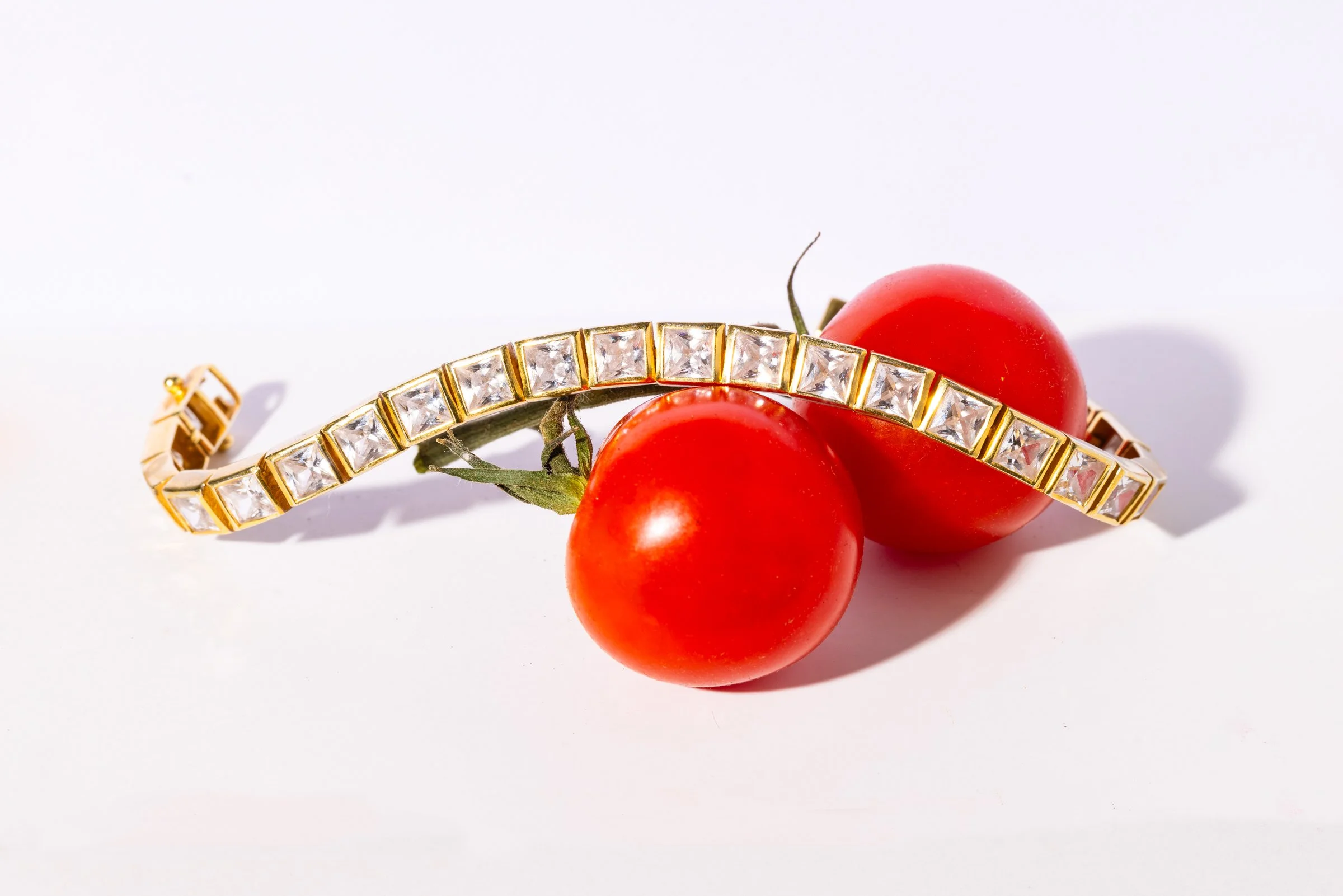 Two cherry tomatoes with a gold bracelet decorated with clear gemstones resting on top.