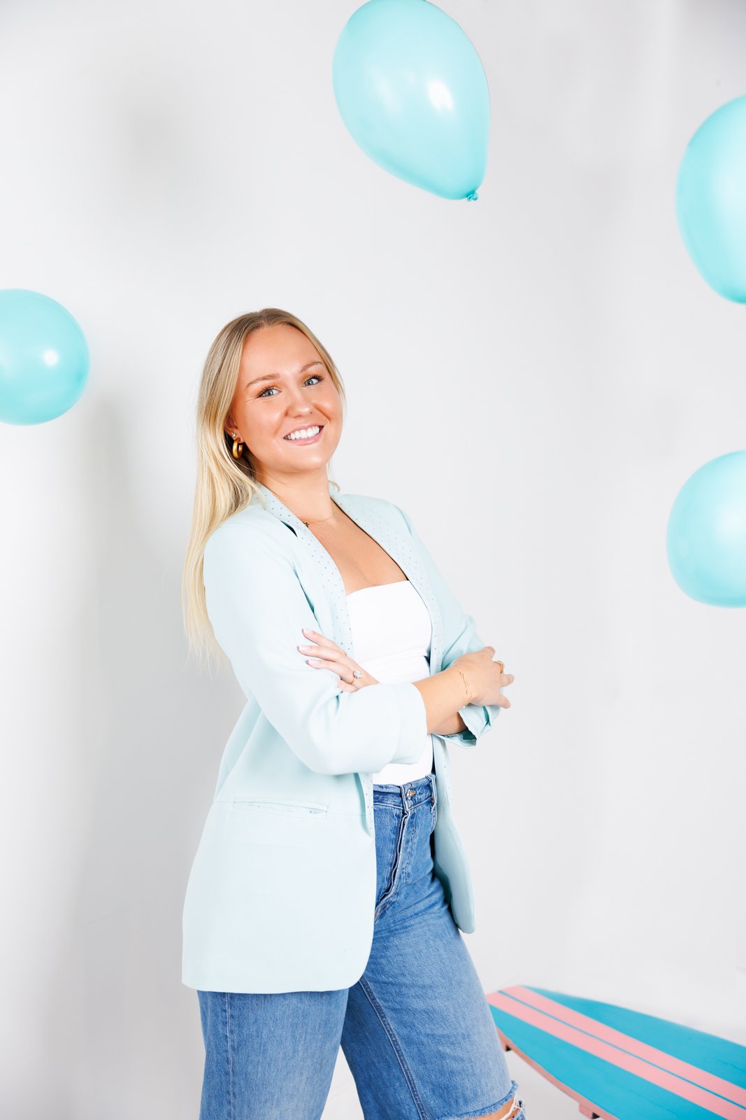 Woman in light blue blazer and jeans smiling at camera with blue balloons around her