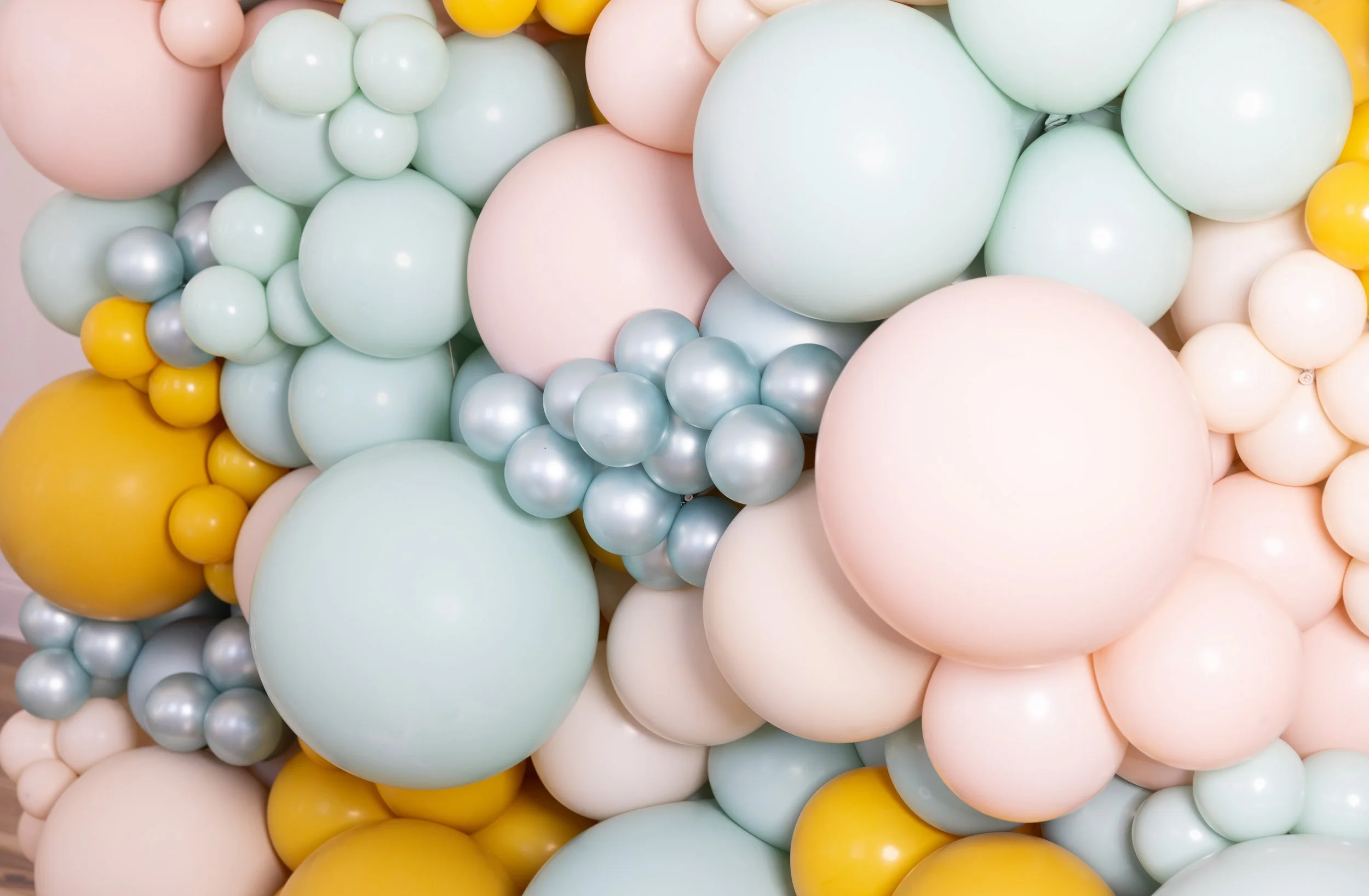 A cluster of pastel-colored balloons in shades of mint green, light pink, yellow, white, and silver.