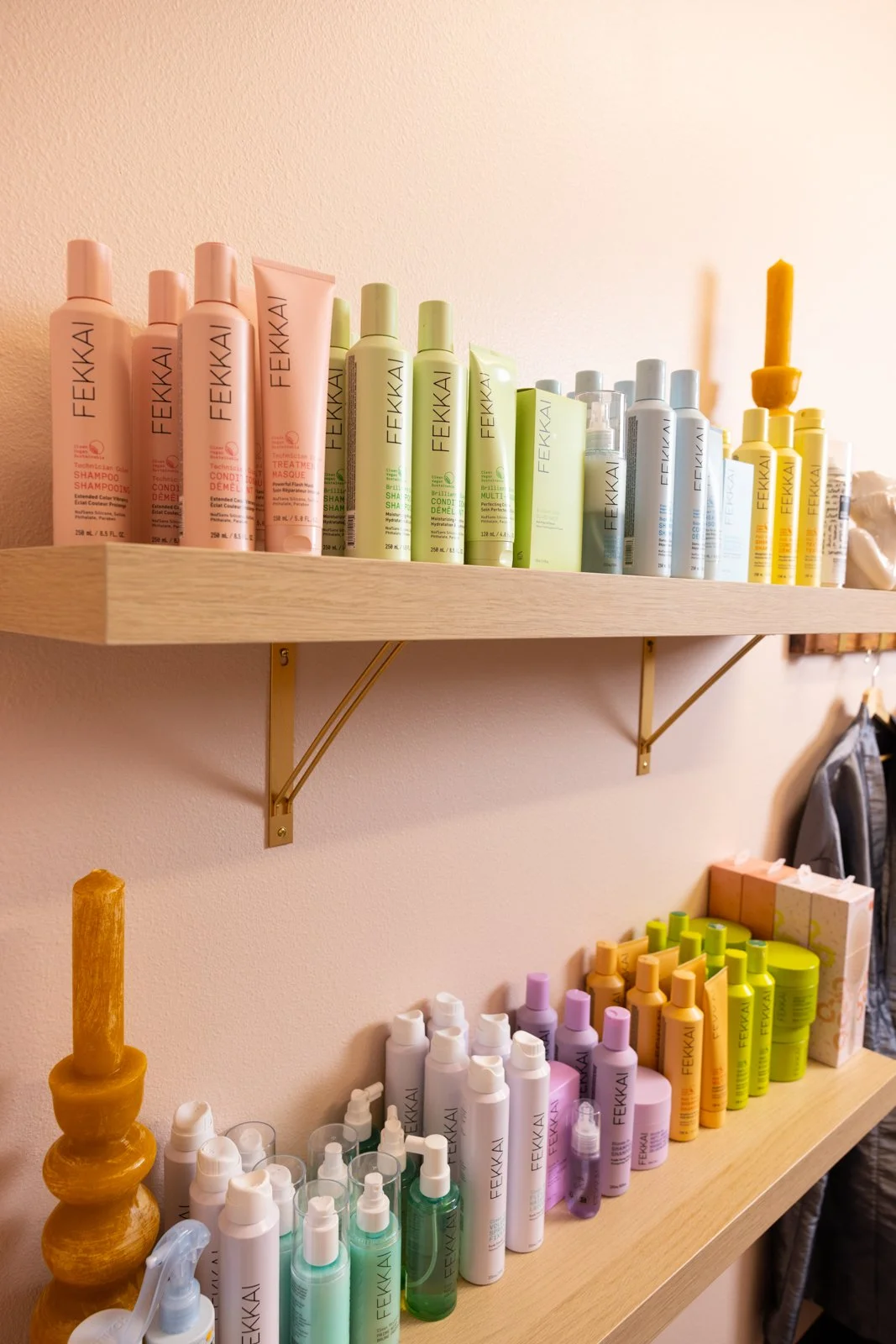 Shelves with bottles of hair care products in different pastel colors, arranged in a row in a salon or store.
