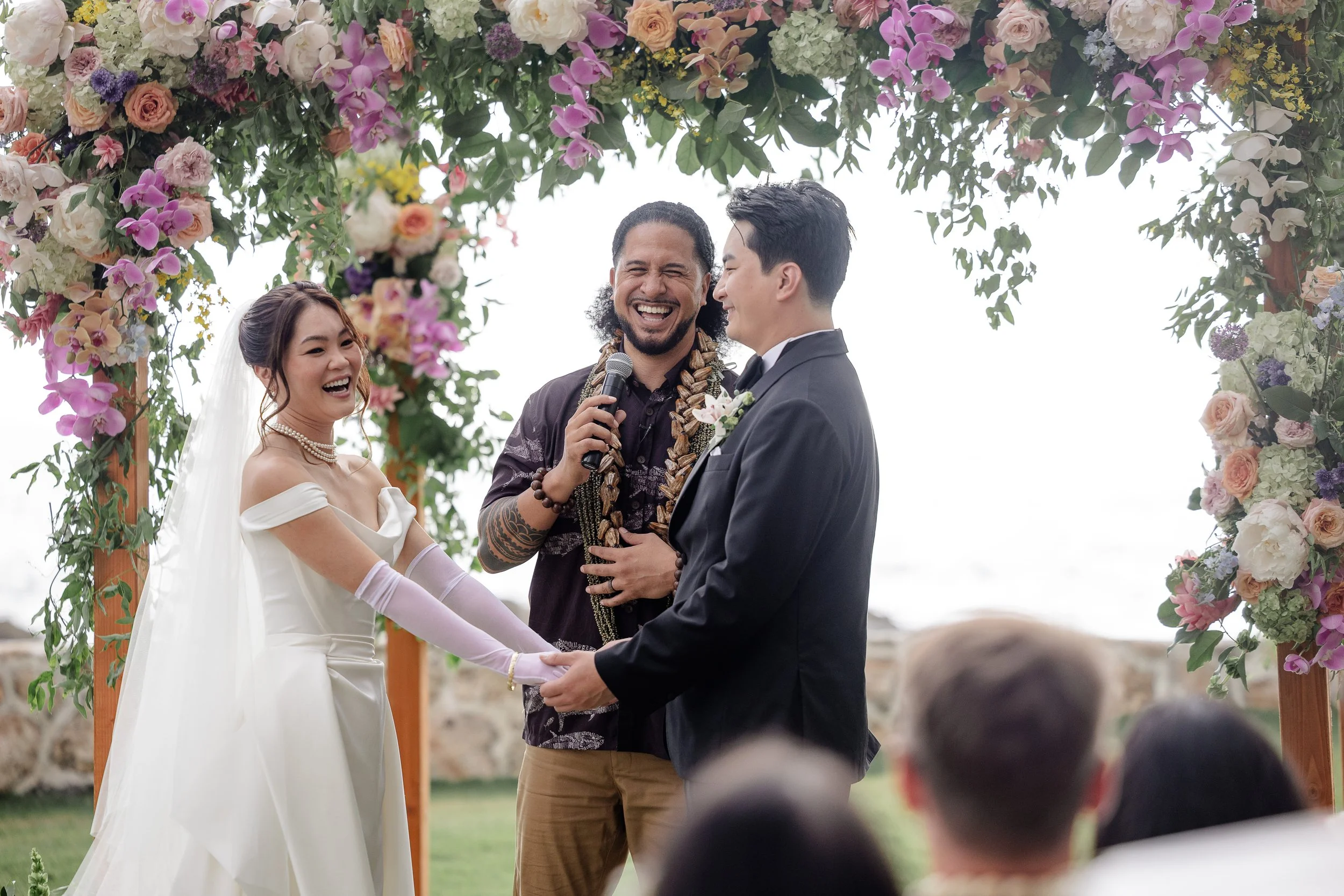 bride and groom at the alter holding hands across from each other while smiling at each other and wedding officiant laughing with them