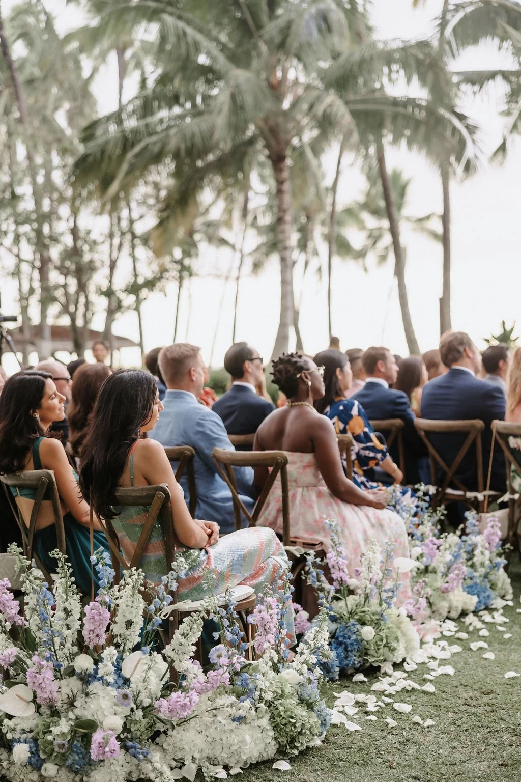 Guests sit at Hawaii wedding ceremony with flower arrangements lining a wavy aisle.