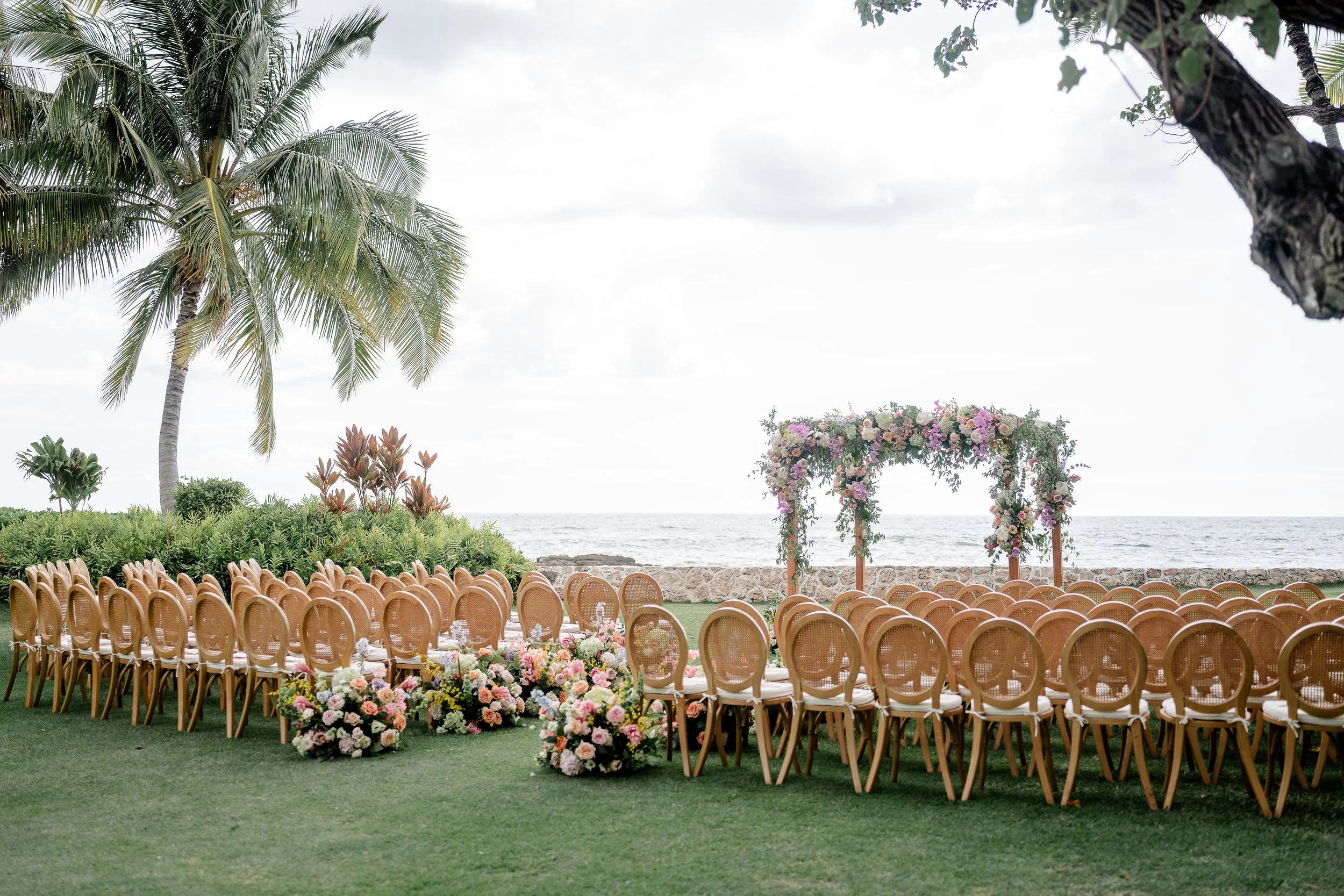 all ceremony chairs facing the ocean and wooden alter structure with vibrant cascading flowers