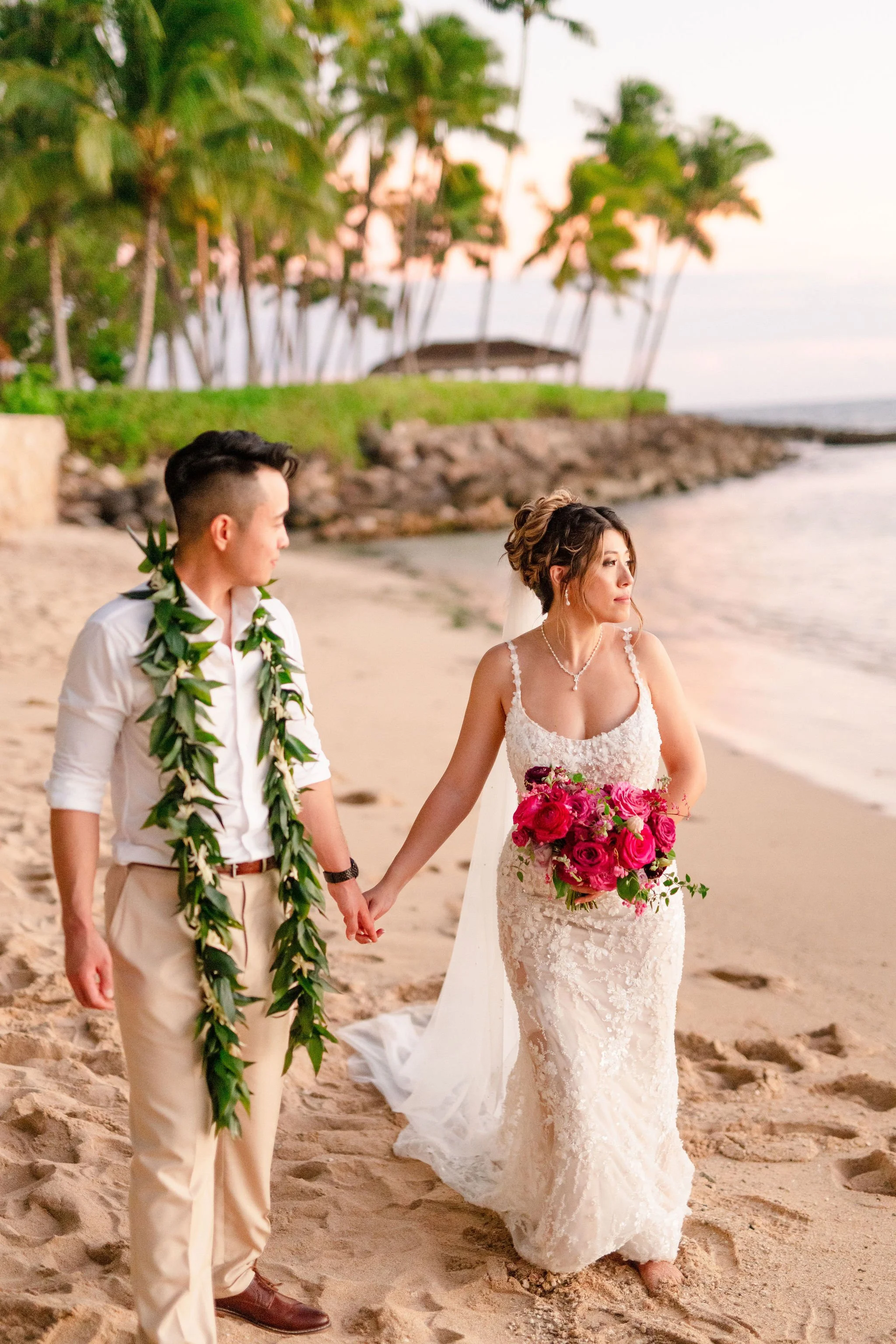 bride and groom holding hands walking down the beach in hawaii