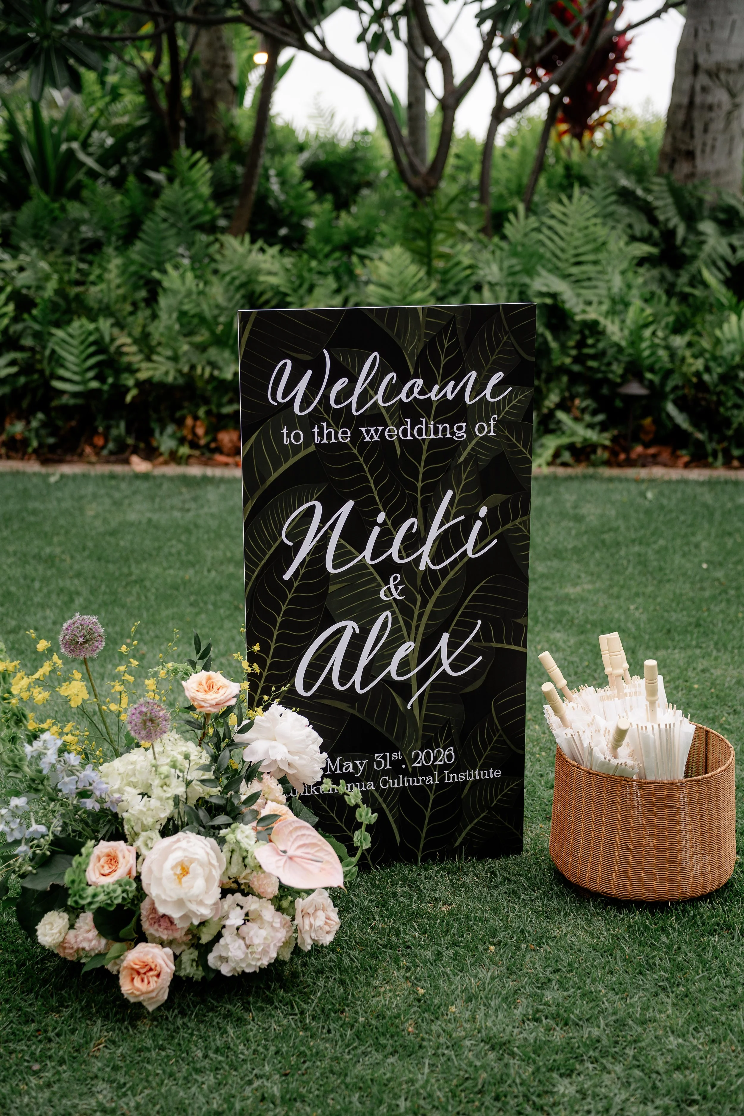 welcome sign with couples name with flower display on the side and parasols in a basket