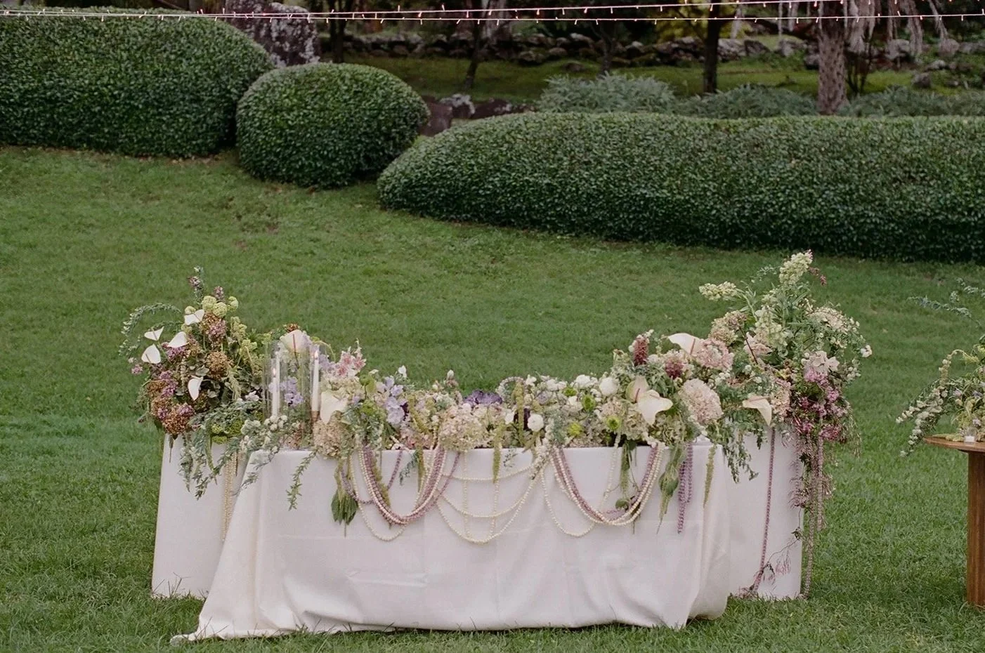 Hawaii wedding planner Love Letter Weddings styled this sweetheart table with tropical green, purple, and white florals and gold taper candles for a Paliku Gardens wedding