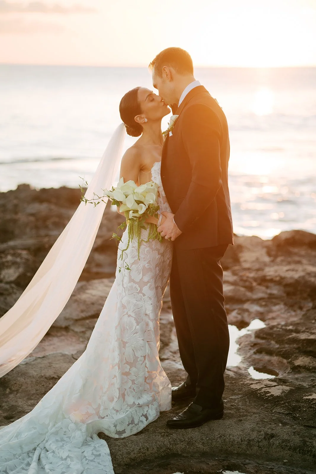 bride and groom kissing in front of sunset in hawaii