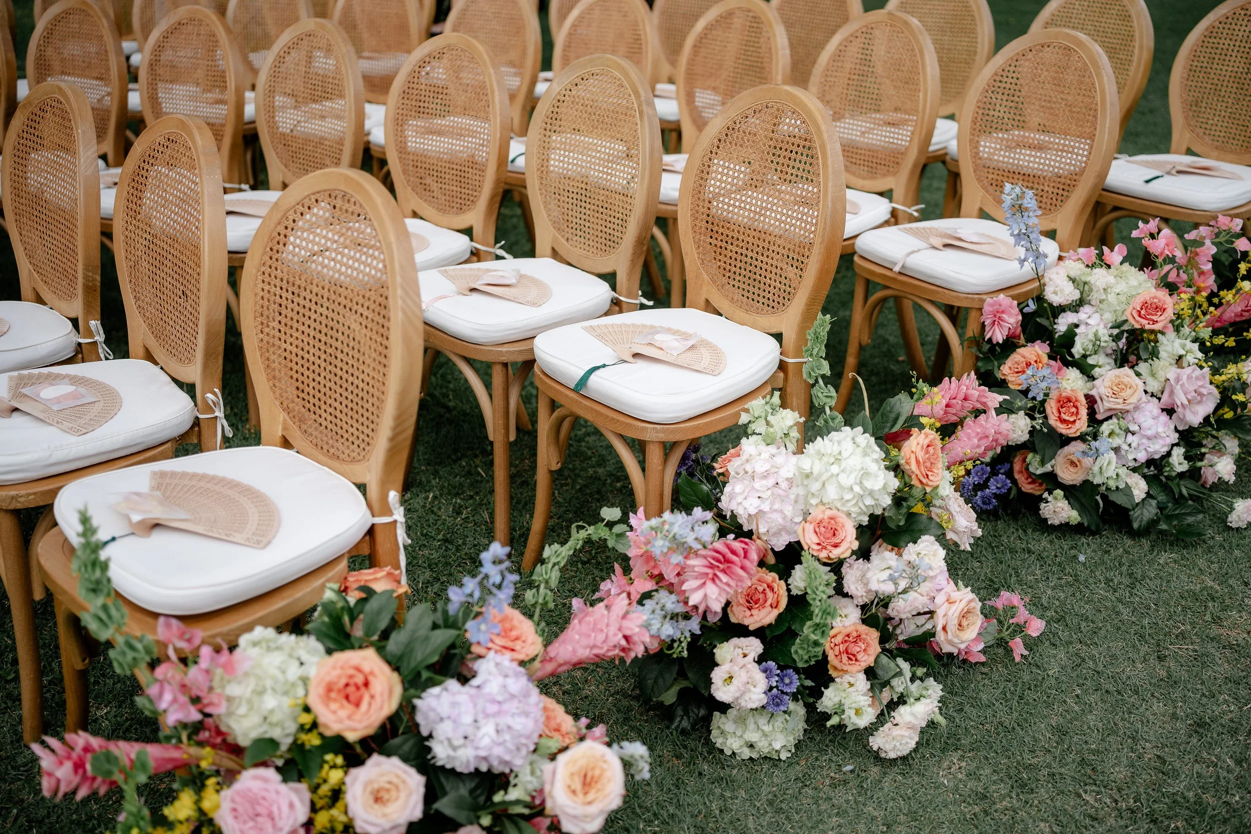 ceremony chairs with hand fans on seats with flower arrangements for aisle markers