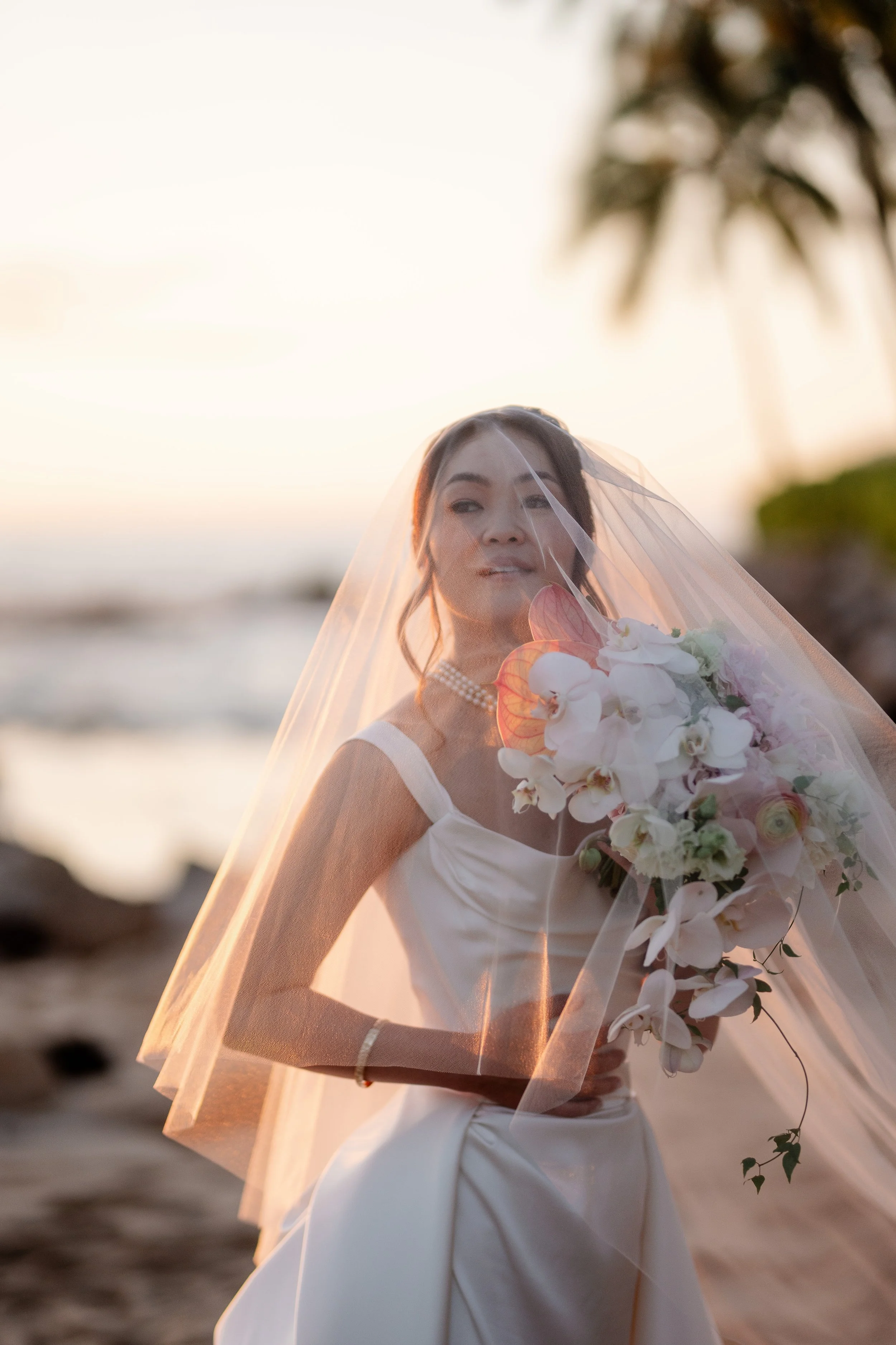 portrait of bride on the beach holding bouquet with veil draping over their face