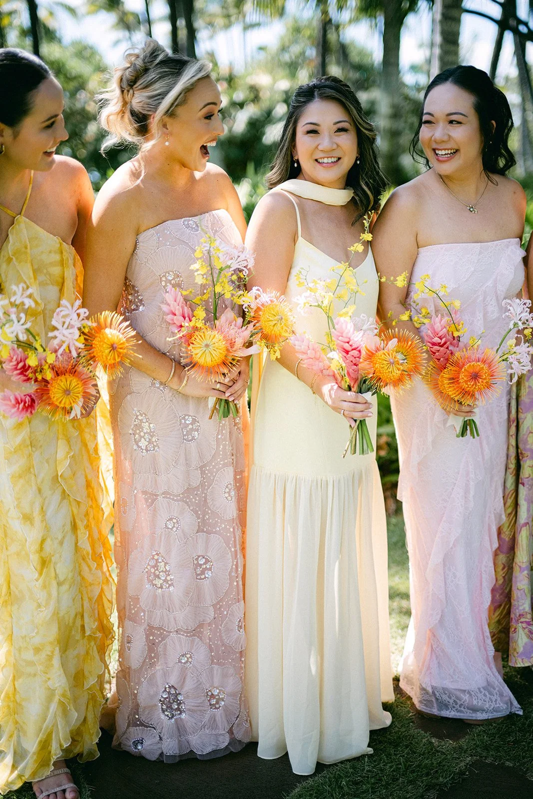Outdoor wedding ceremony setup with rows of chairs decorated with white garlands, a floral arch with pink and peach flowers, and a background of palm trees and a grassy lawn.