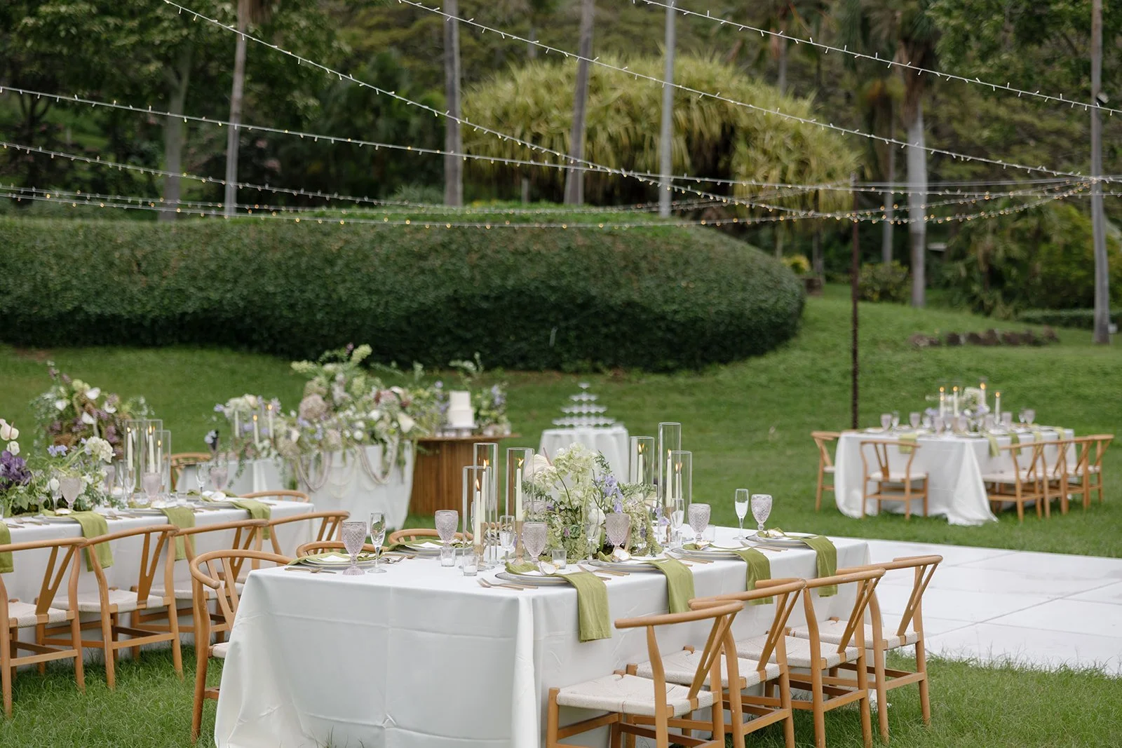 Oahu wedding planner Love Letter Weddings designed this reception with long tables, wishbone chairs, and a champagne tower under twinkle lights at Paliku Gardens