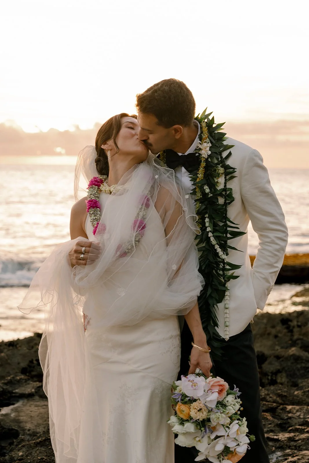 bride and groom kissing in front of sunset in hawaii