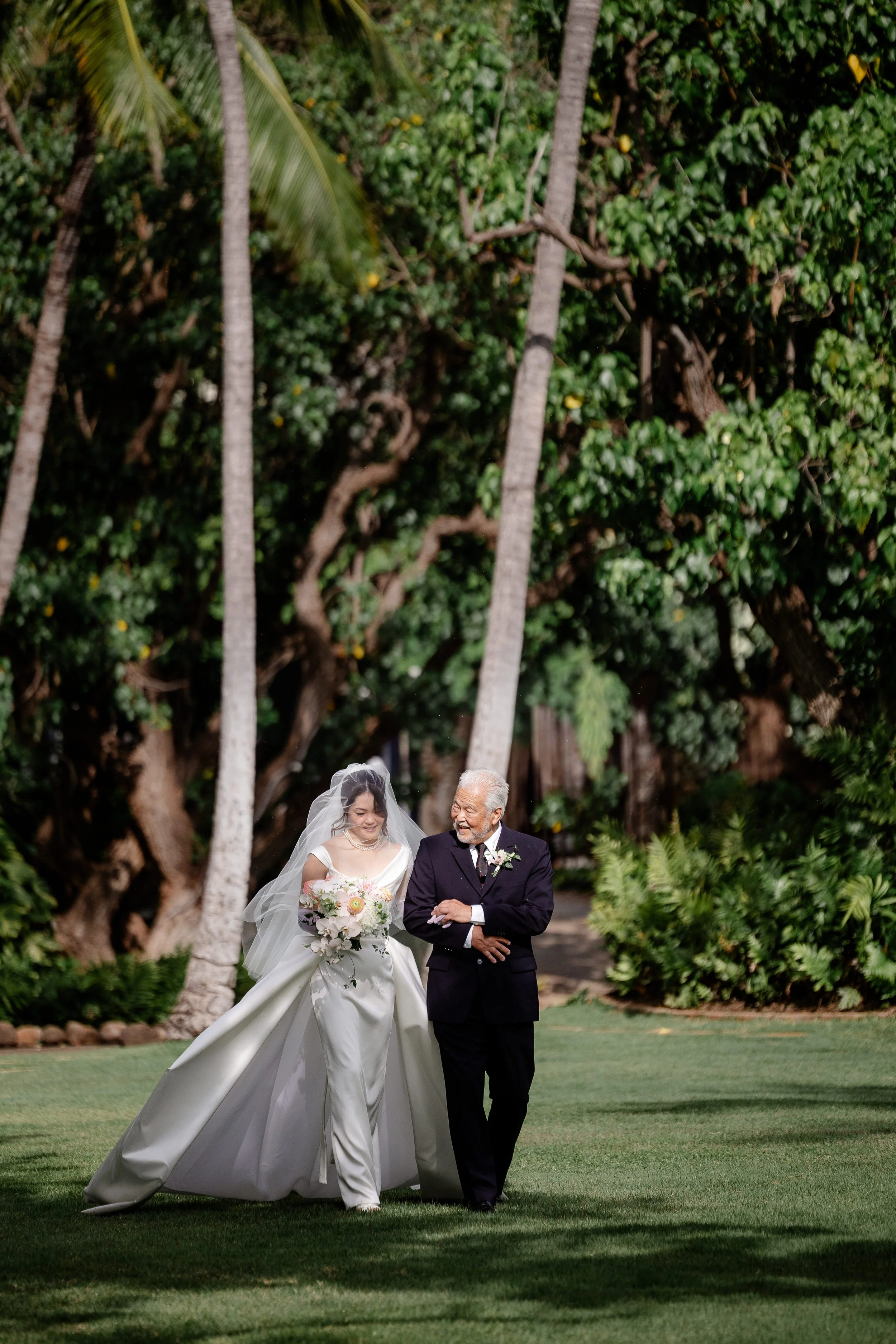 bride in elegant white dress holding a bouquet, linking arms with smiling father walking down the aisle