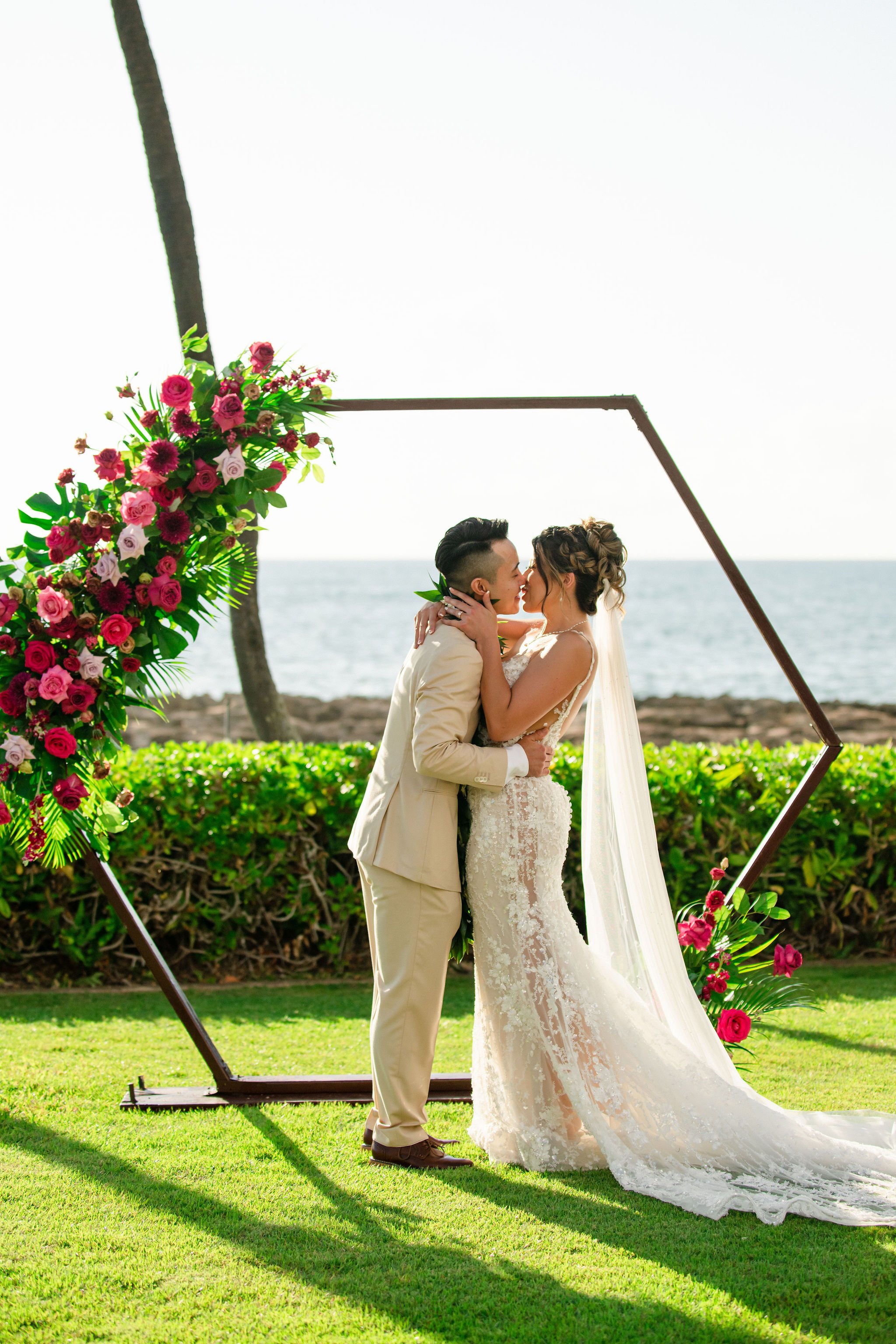 bride and groom kissing in front of altar near a beach in hawaii