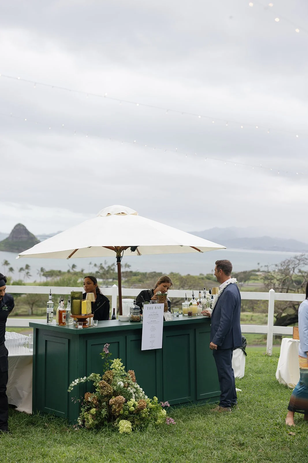 Guest ordering a cocktail at green floral bar front with menu at Paliku Gardens Hawaii wedding