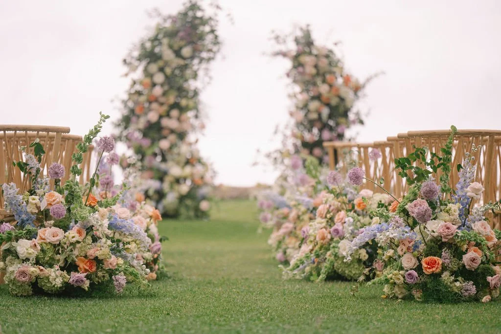 A wedding ceremony outdoors with a bride and groom holding hands in front of a lush green landscape and palm trees, and a separate image of bridesmaids in gray dresses holding bouquets outdoors near a floral arch.