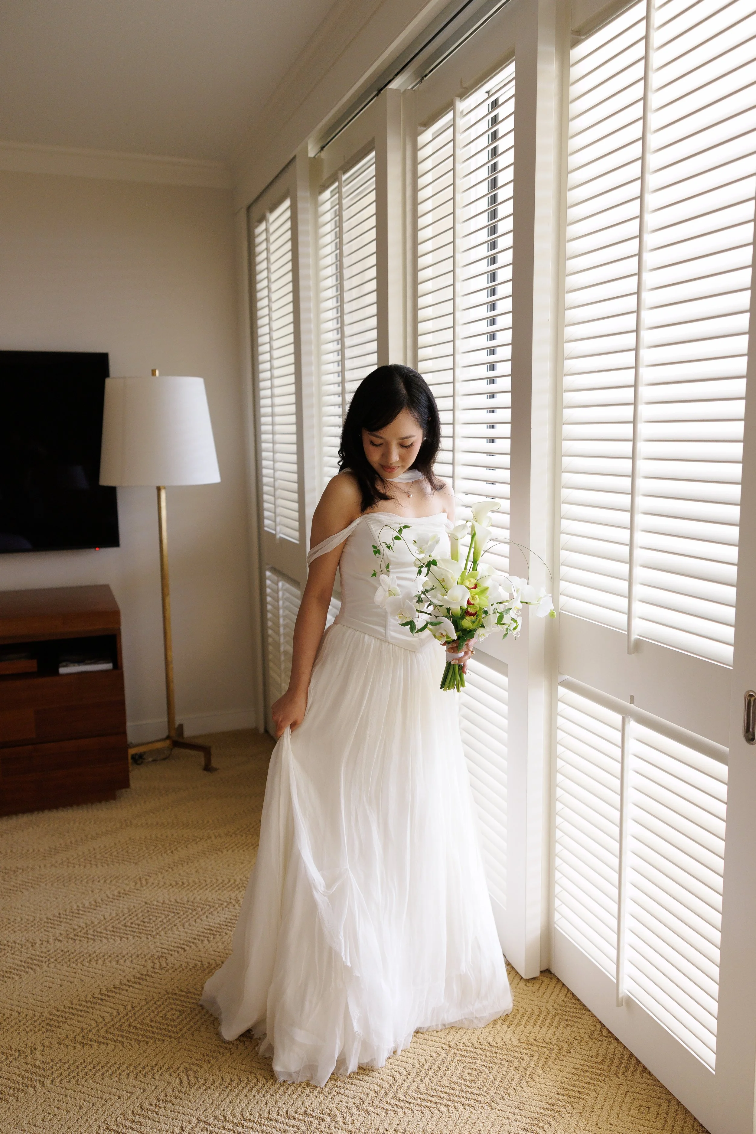 bride holding bouquet and admiring dress for getting ready photo