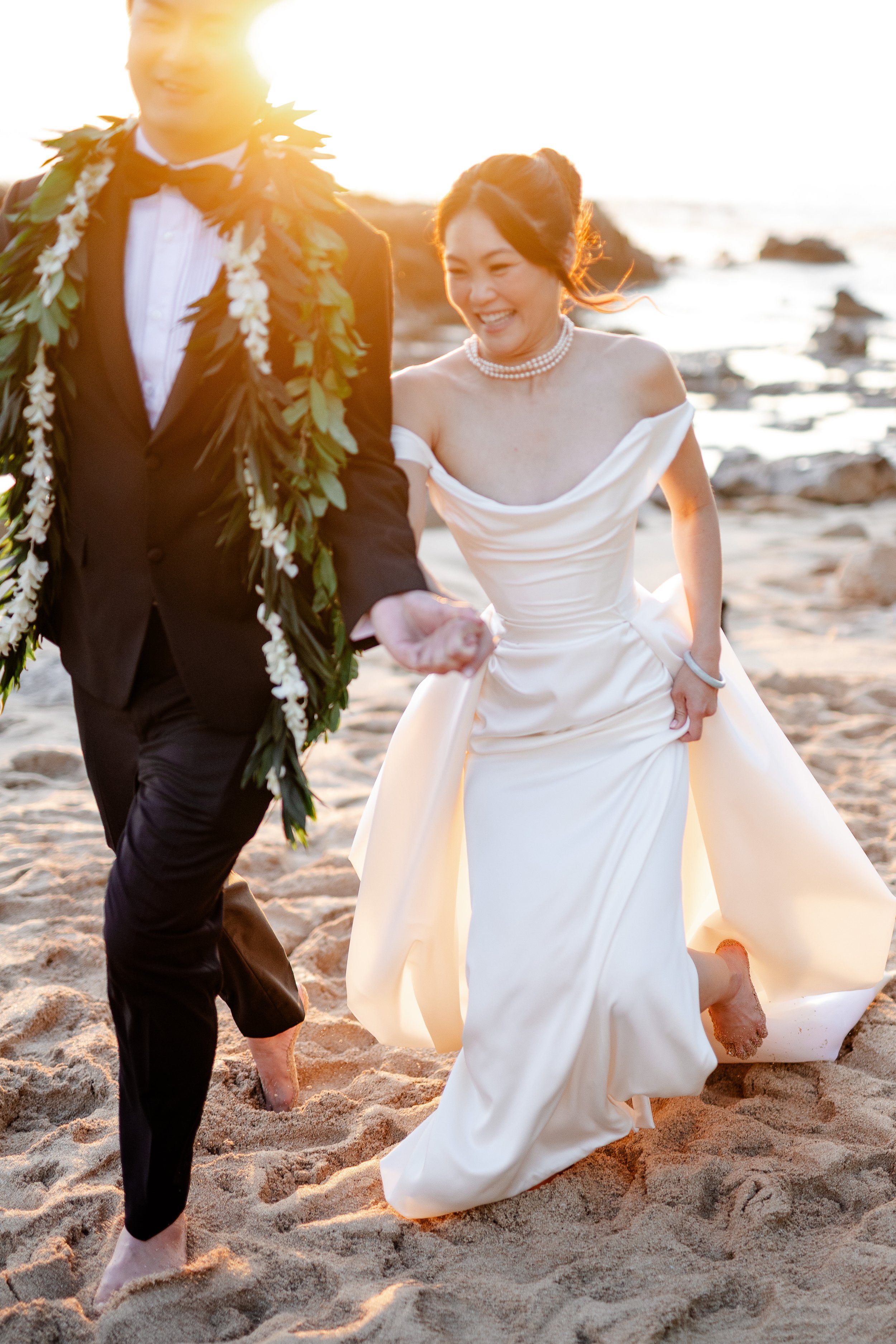 bride and groom smiling, holding hands, and running on the beach