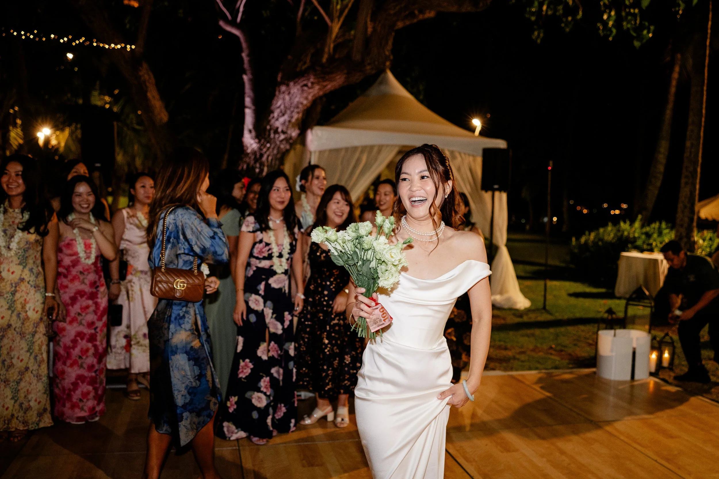 bride holding bouquet with female guests waiting behind her to throw garter