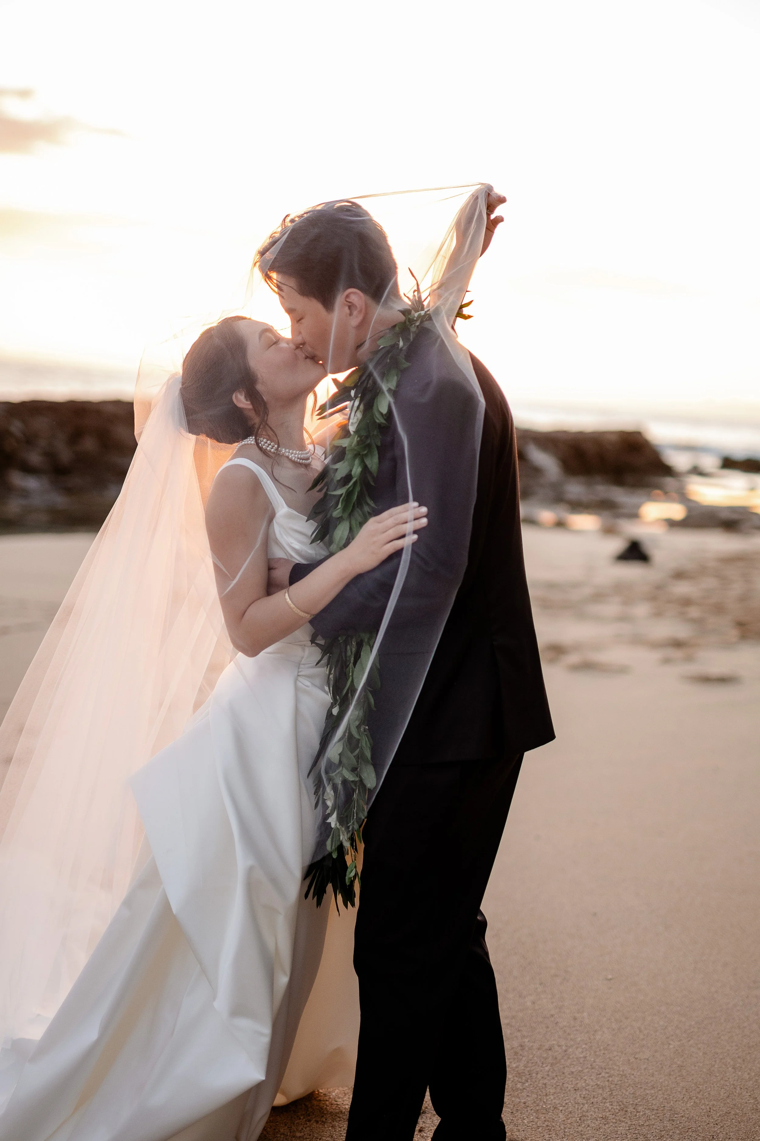 bride and groom kissing under brides veil on the beach