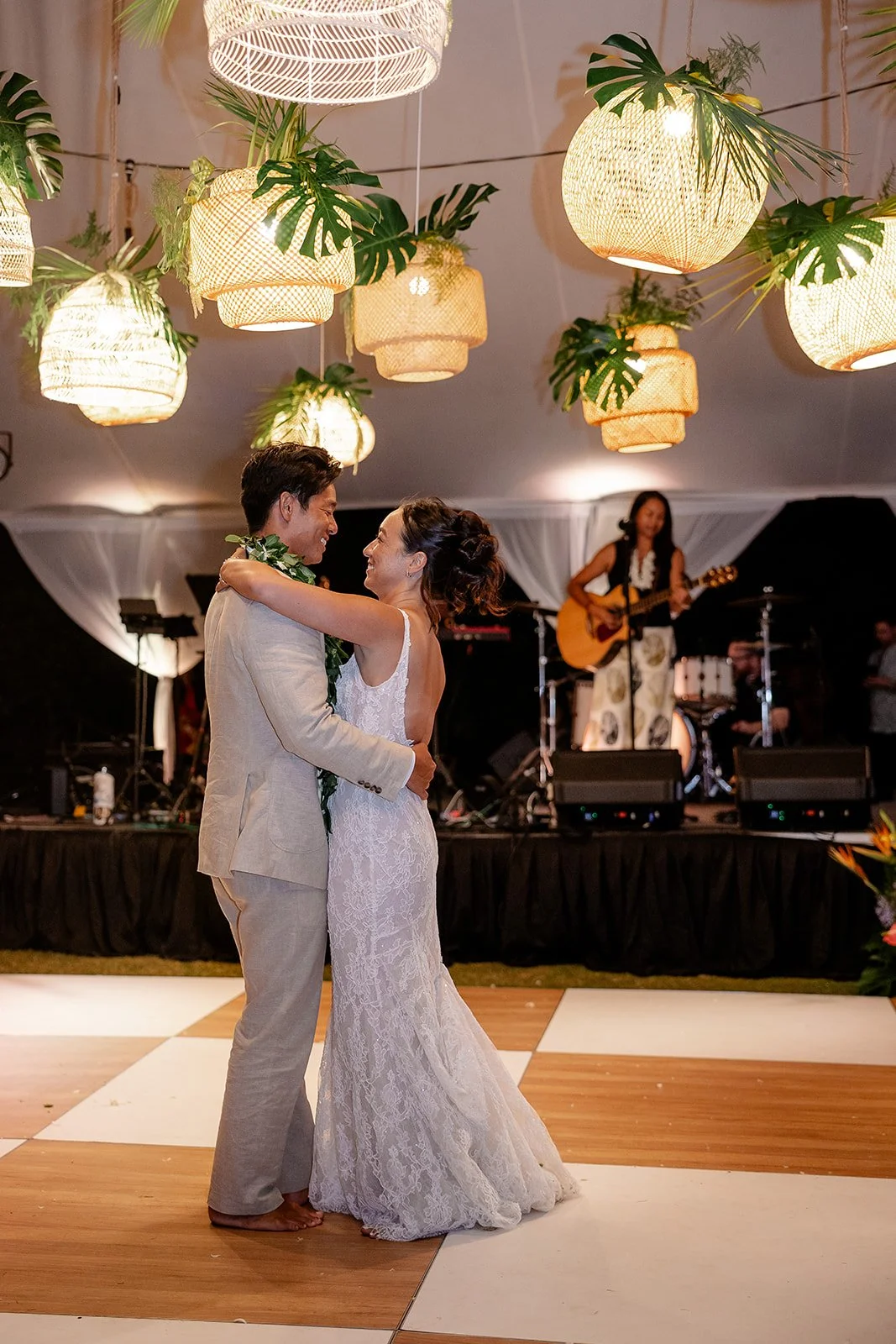 bride and groom under rattan lanterns with greenery