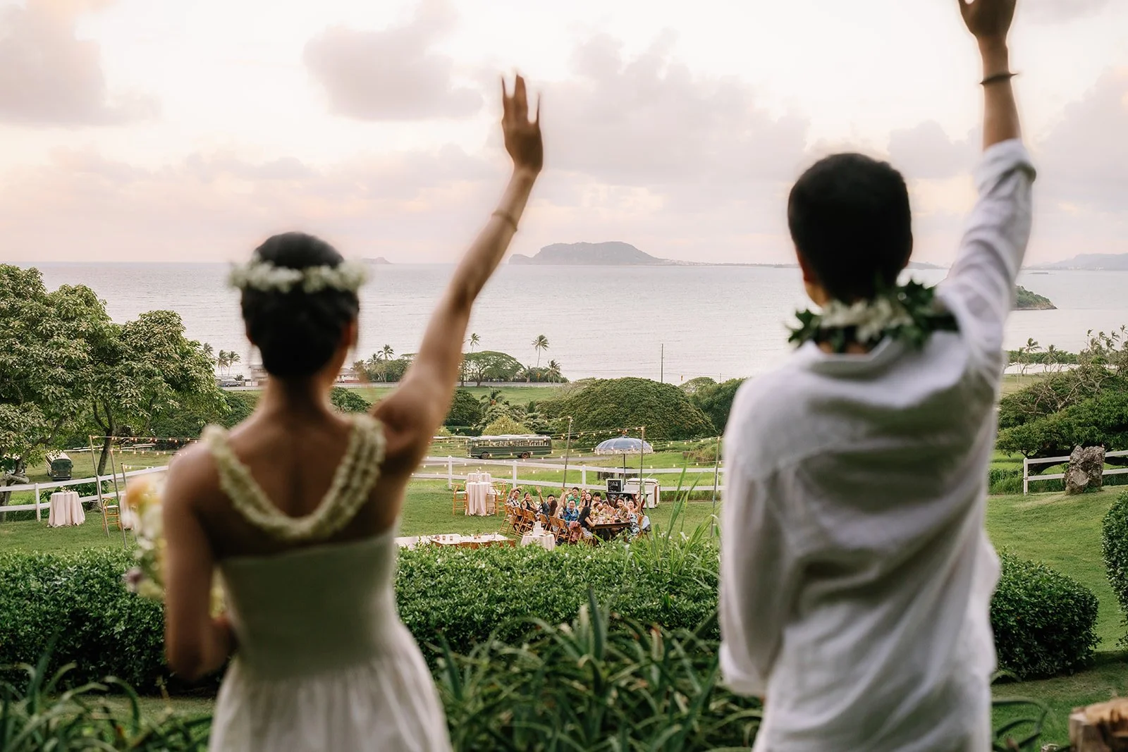 Bride and groom waving high to their guests sitting down at reception