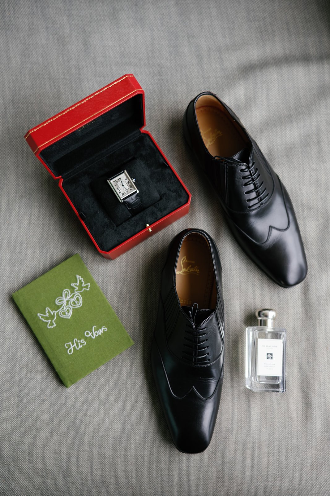Groom's flatlay with shoes, cologne, Cartier watch, and vow book at Paliku Gardens wedding on Oahu