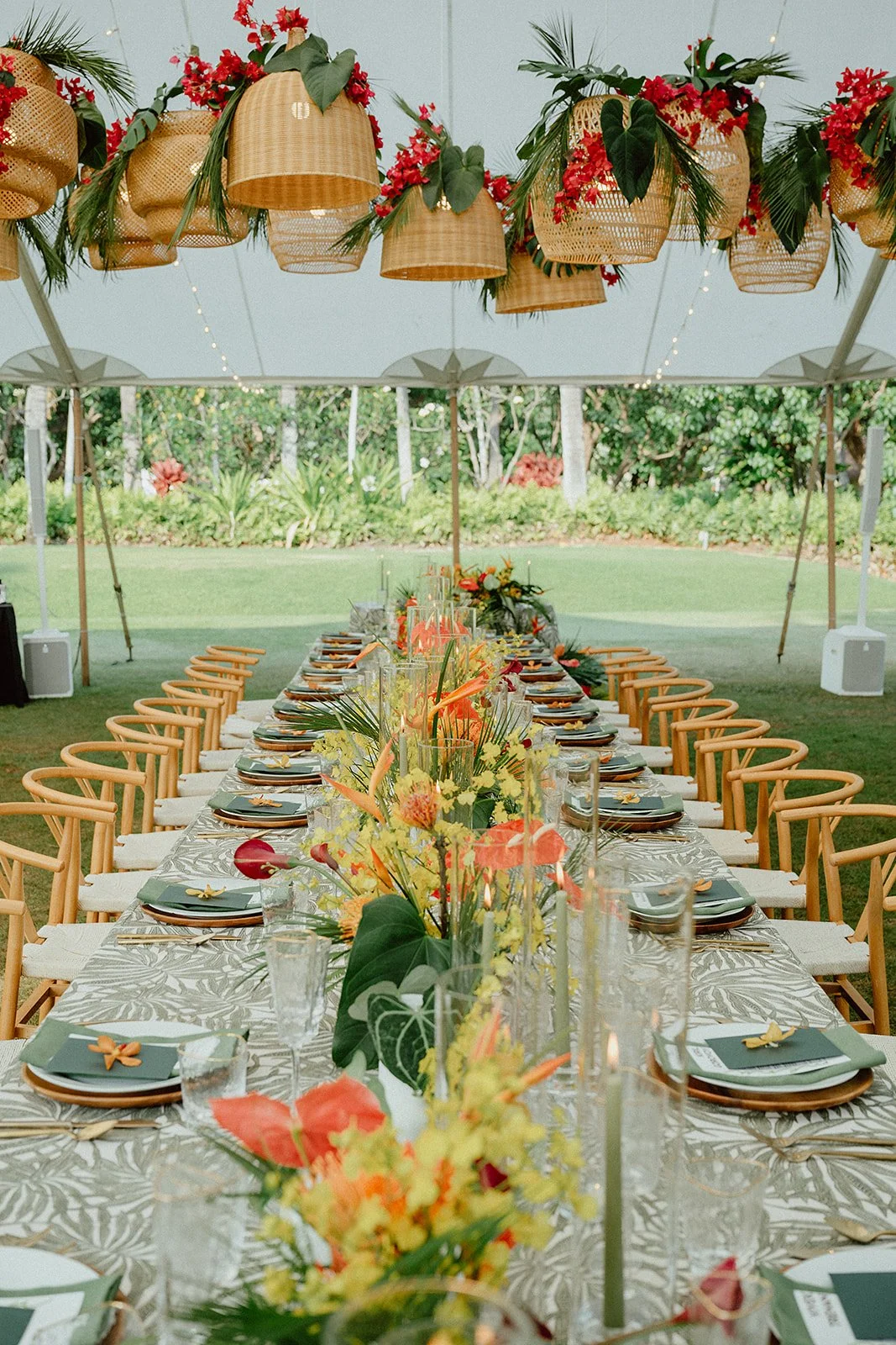 A beautifully arranged wedding place setting with a personalized name card on dinner plates, floral accents, and hanging rattan lanterns inside a giant white tent