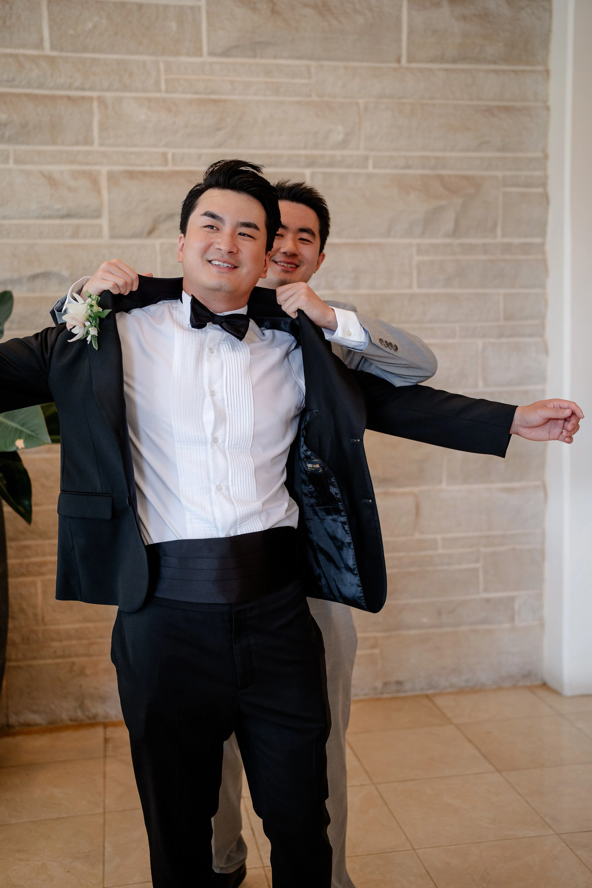 gentleman assisting groom putting on suit jacket