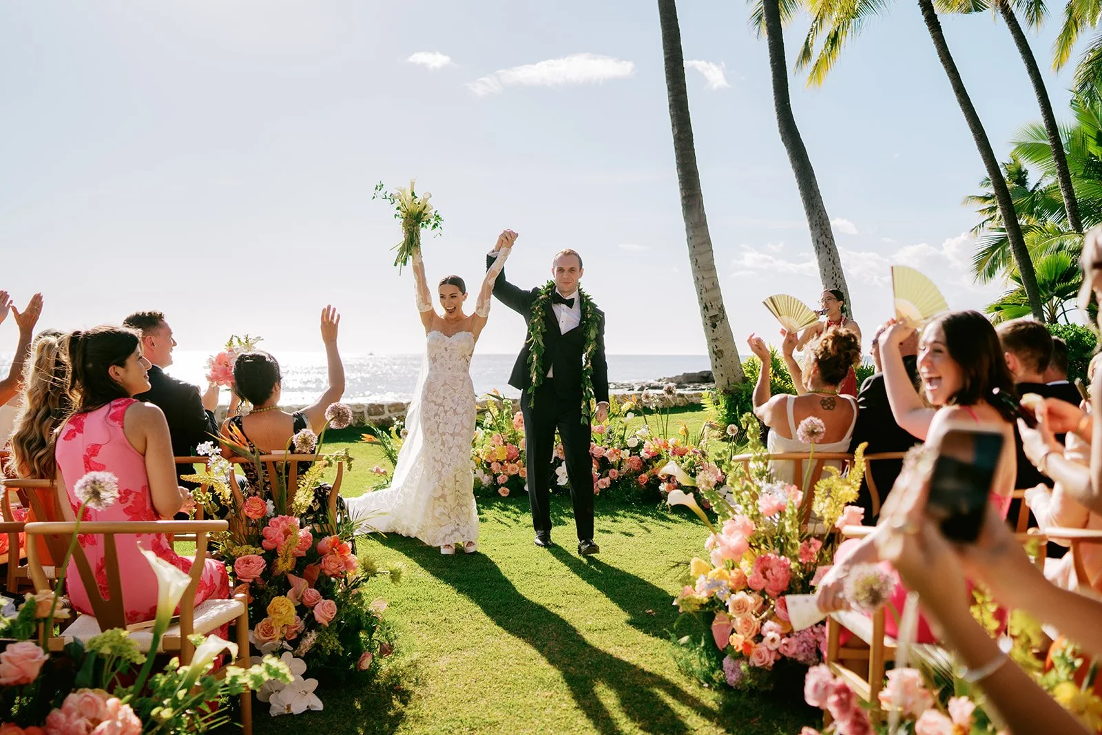 bride and groom cheering as they walk down the aisle in hawaii