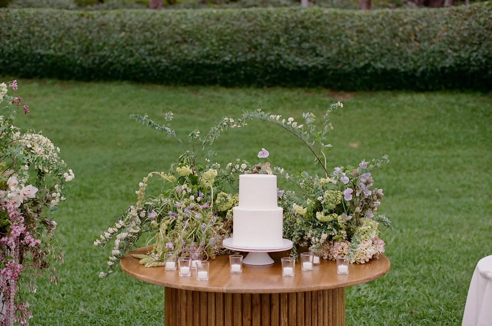 Two tier wedding cake on a floral meadow tablescape with tealight candles, styled by Oahu wedding planner Love Letter Weddings at Paliku Gardens
