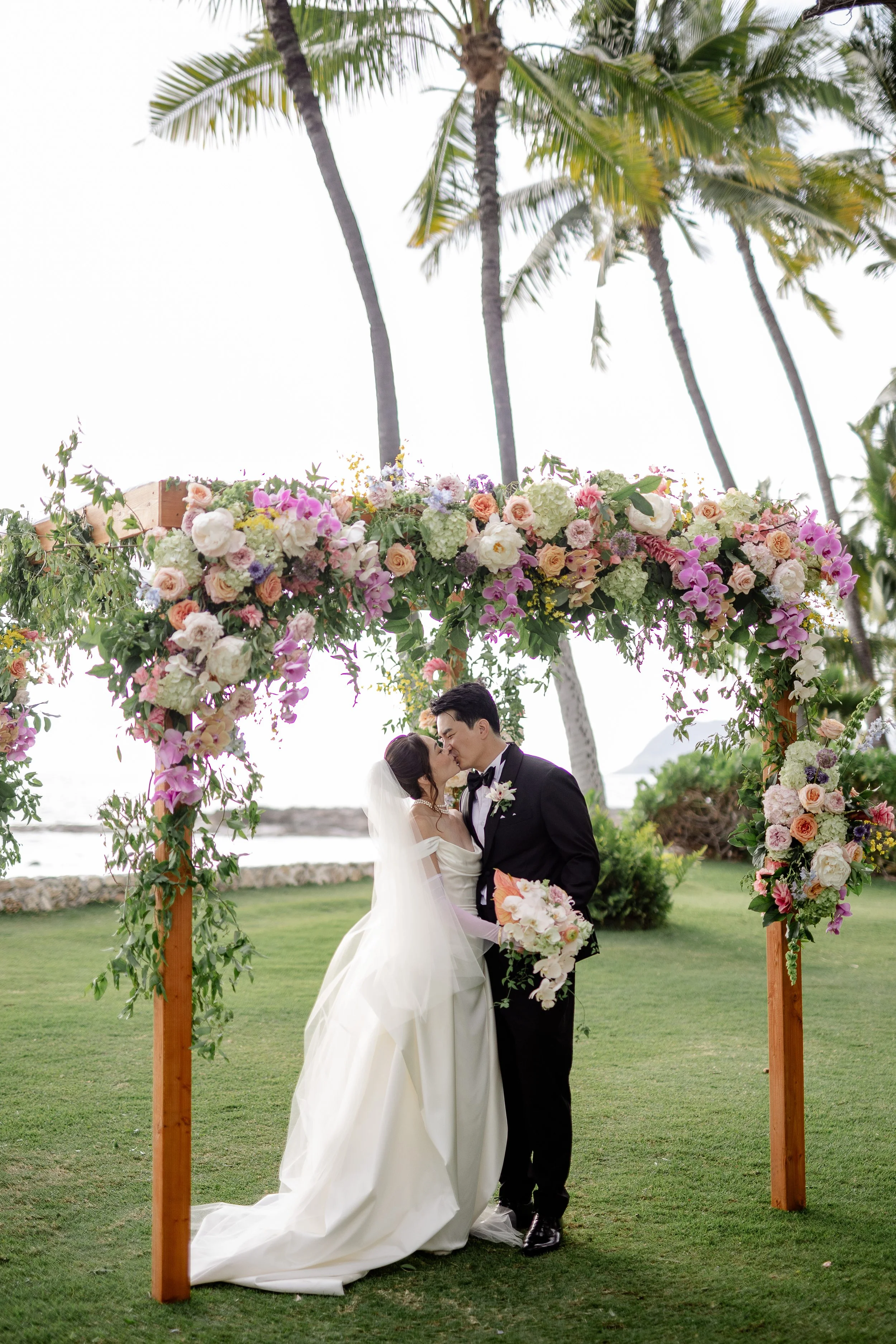 bride and groom kissing under wooden square alter with cascading flowers