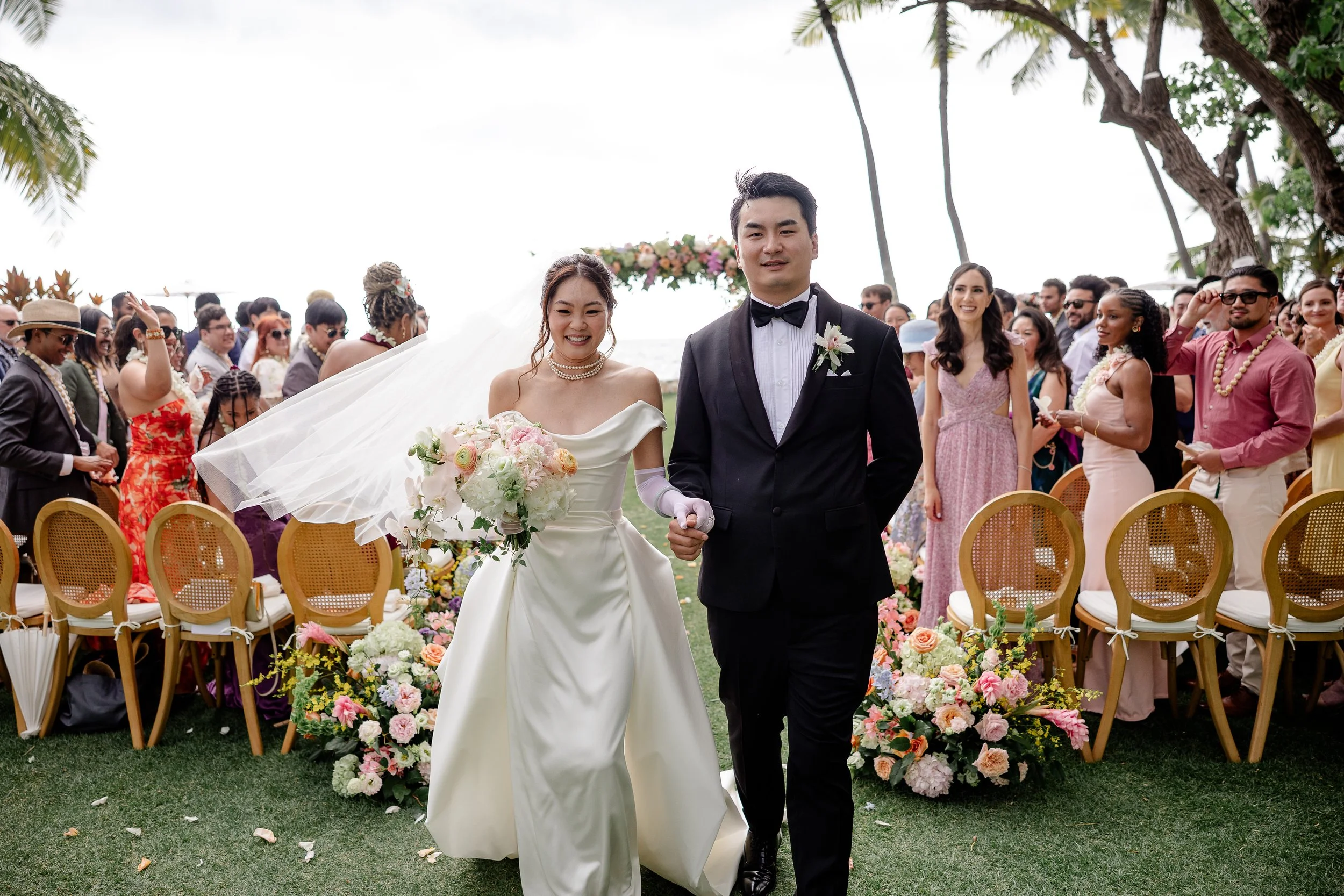 bride and groom holding hands walking down aisle with big smiles as guests are standing  in front of their chairs to the left and right of the couple
