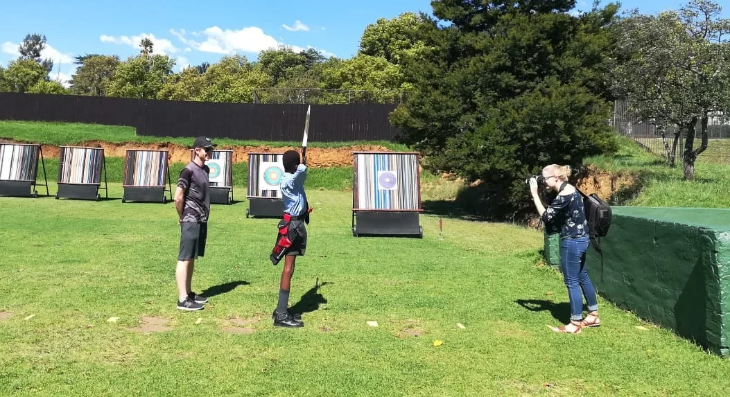 Above: Olufemi Oyeka takes aim at a target while coach Alistair observes and Sarah Koning takes photographs at the Archers of Zoolake archery range.
