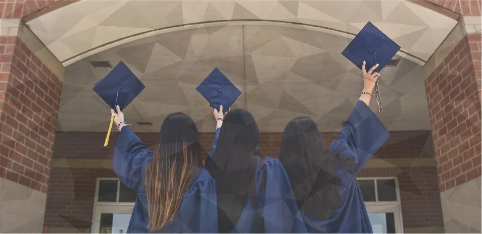 Grads are celebrating by throwing their hats into the air in front of a school.