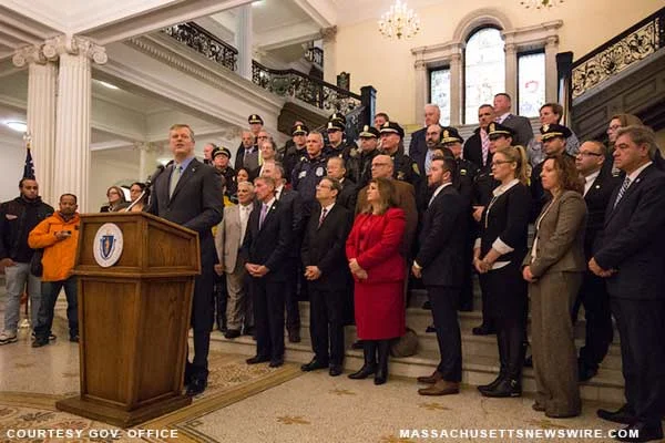 CAPTION: Governor Charlie Baker announces Shannon Grant awards during event at the Statehouse in Boston. Behind him stand legislators, local officials, members of law enforcement (including Boston Police Commissioner William Evans), and other stakeholders. Courtesy Gov. office/website.