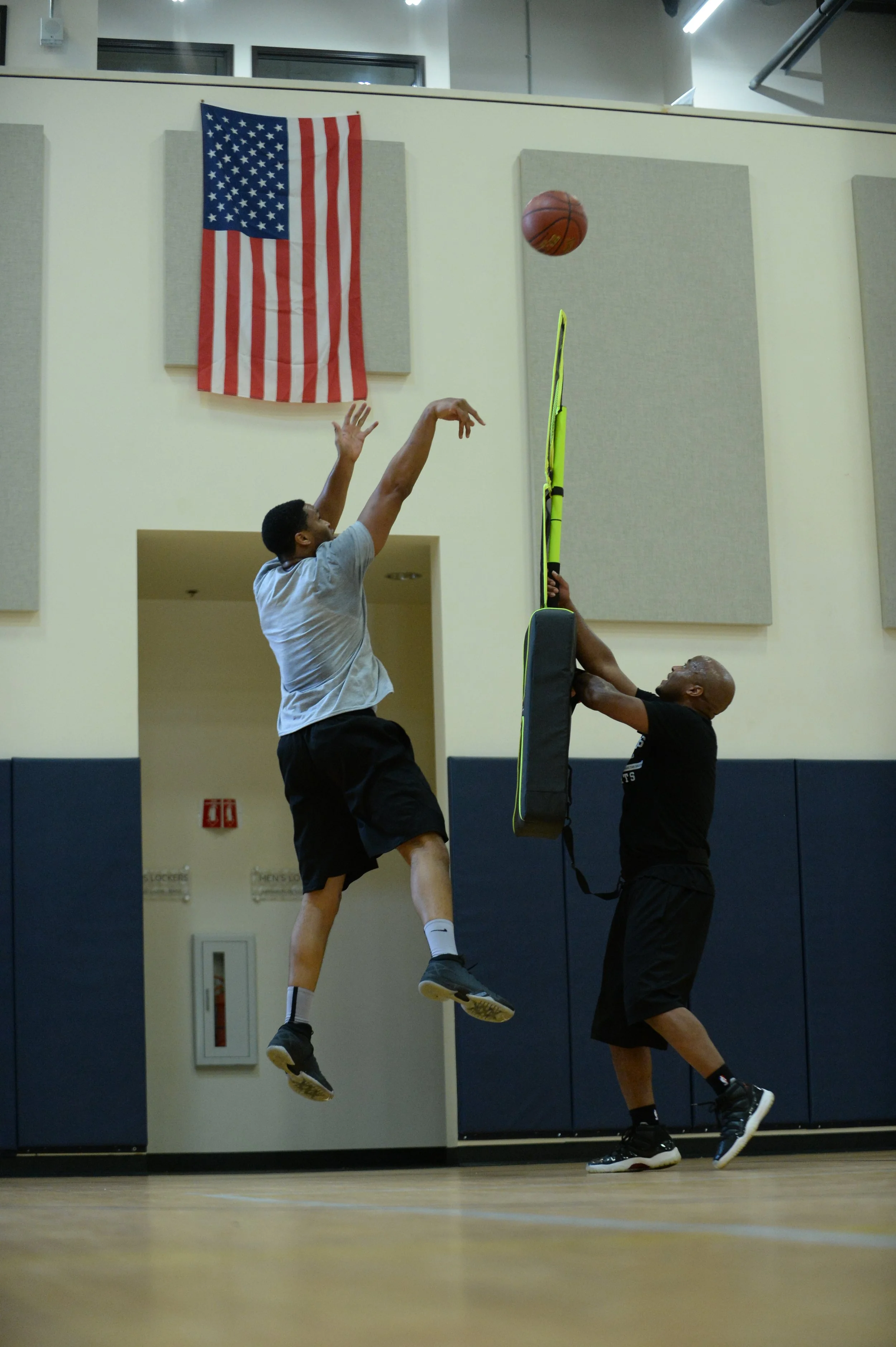 Two basketball players in a gym using the Elite Defender as a basketball training tool for shooting jump shots.