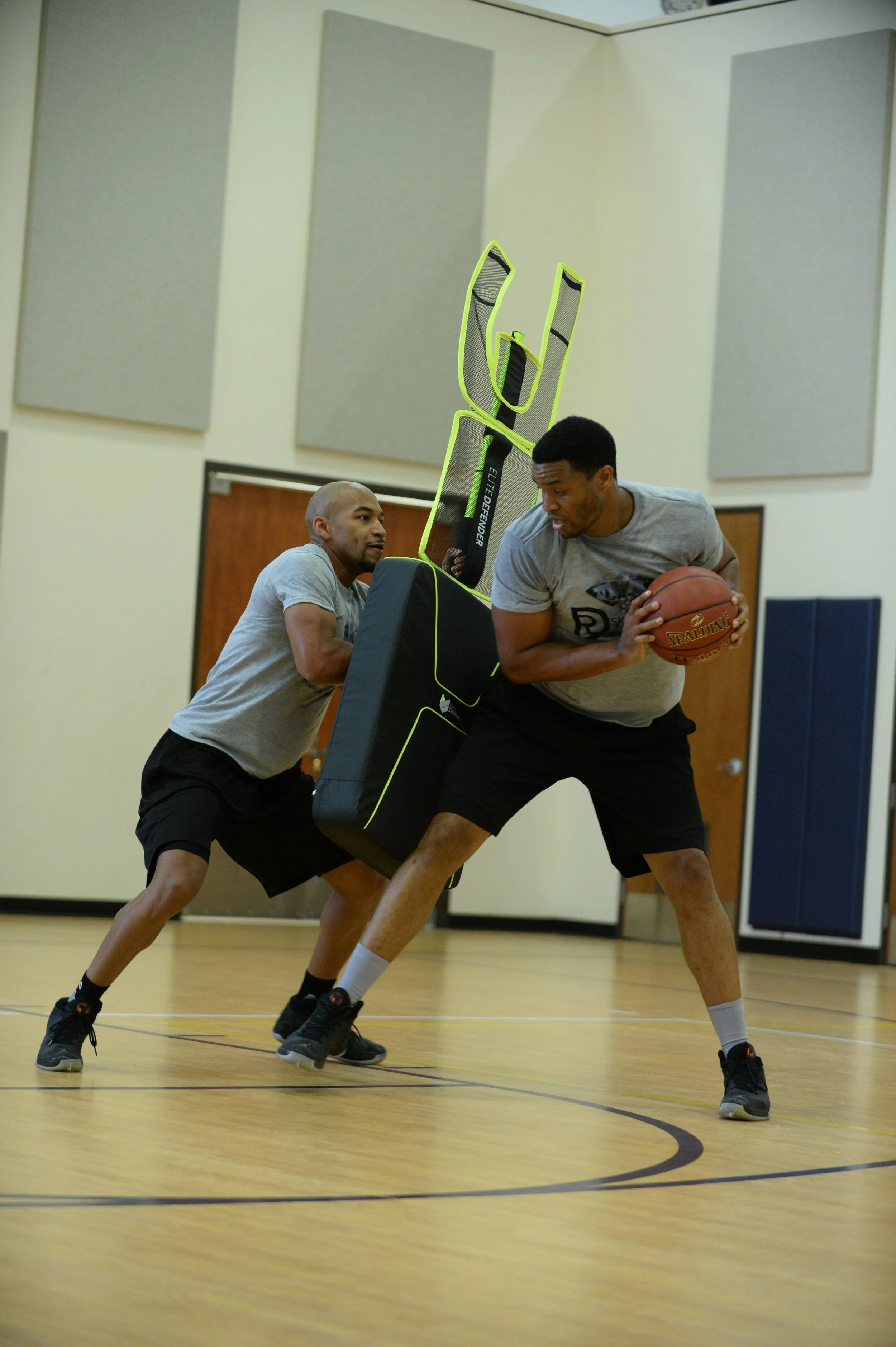 Two basketball players in a gym using the Elite Defender for basketball training for ball handling with contact.