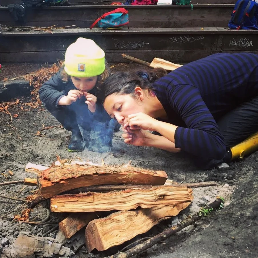 A forest kindergartener works with teacher Liana to reignite a fire using their "fire whistle".